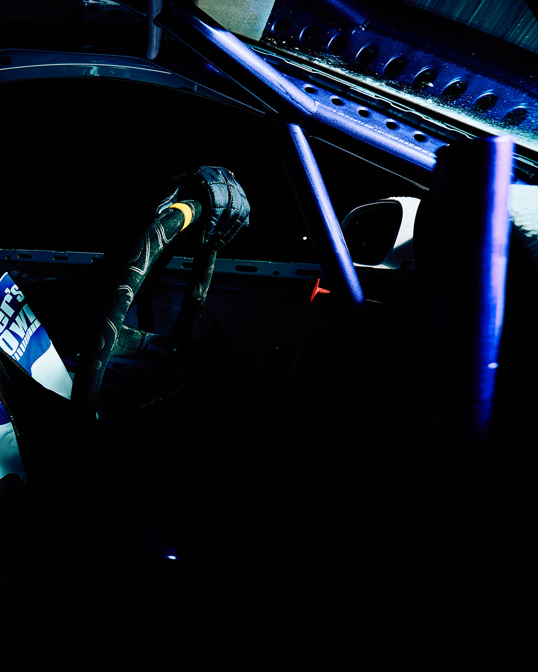 Person in a October's Very Own racing Jacket and helmet inside a car, with visible branding.