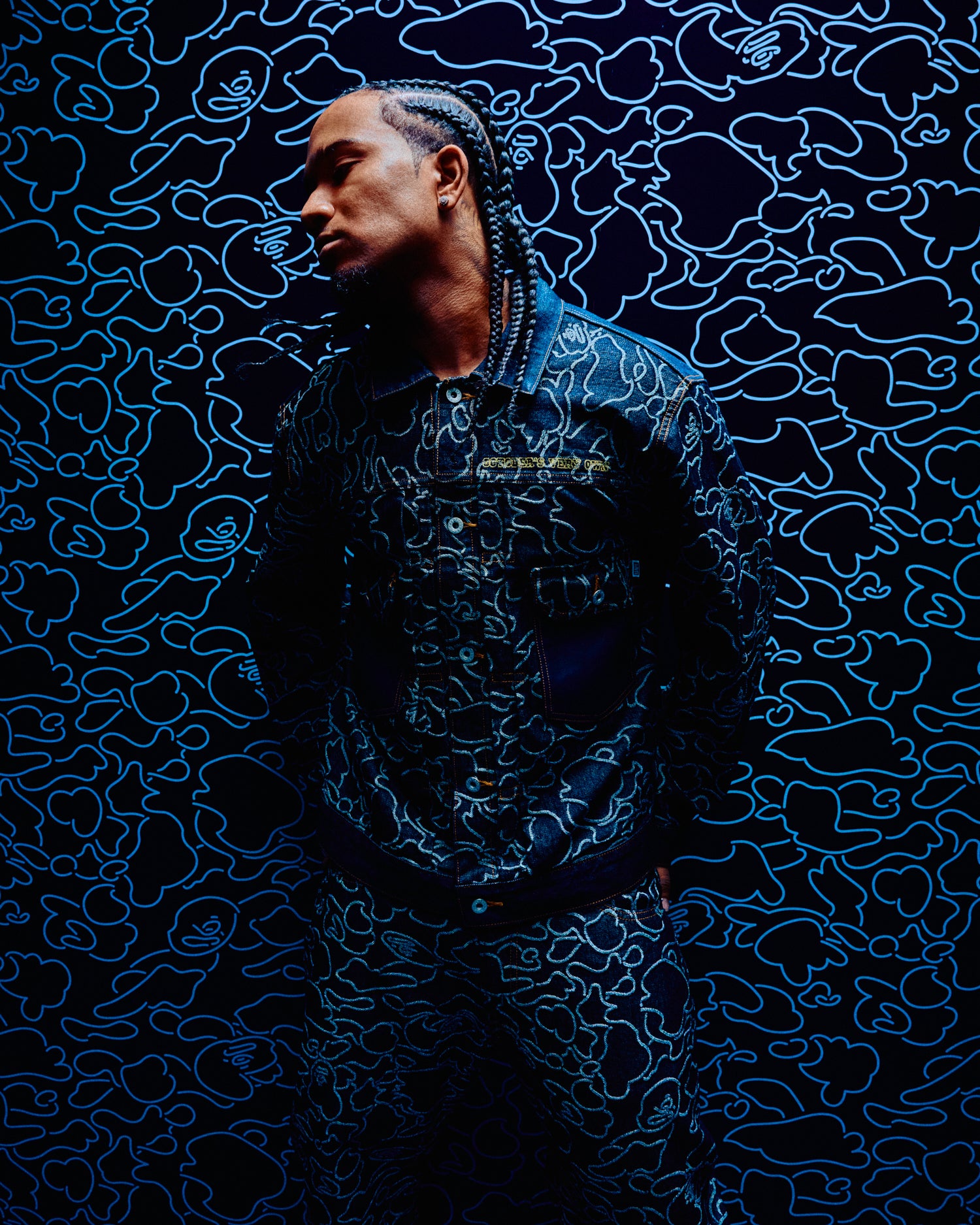 Person wearing a Person wearing a October's Very Own x Bape jacket with text on a blue patterned background jacket with a brand logo against a blue patterned background