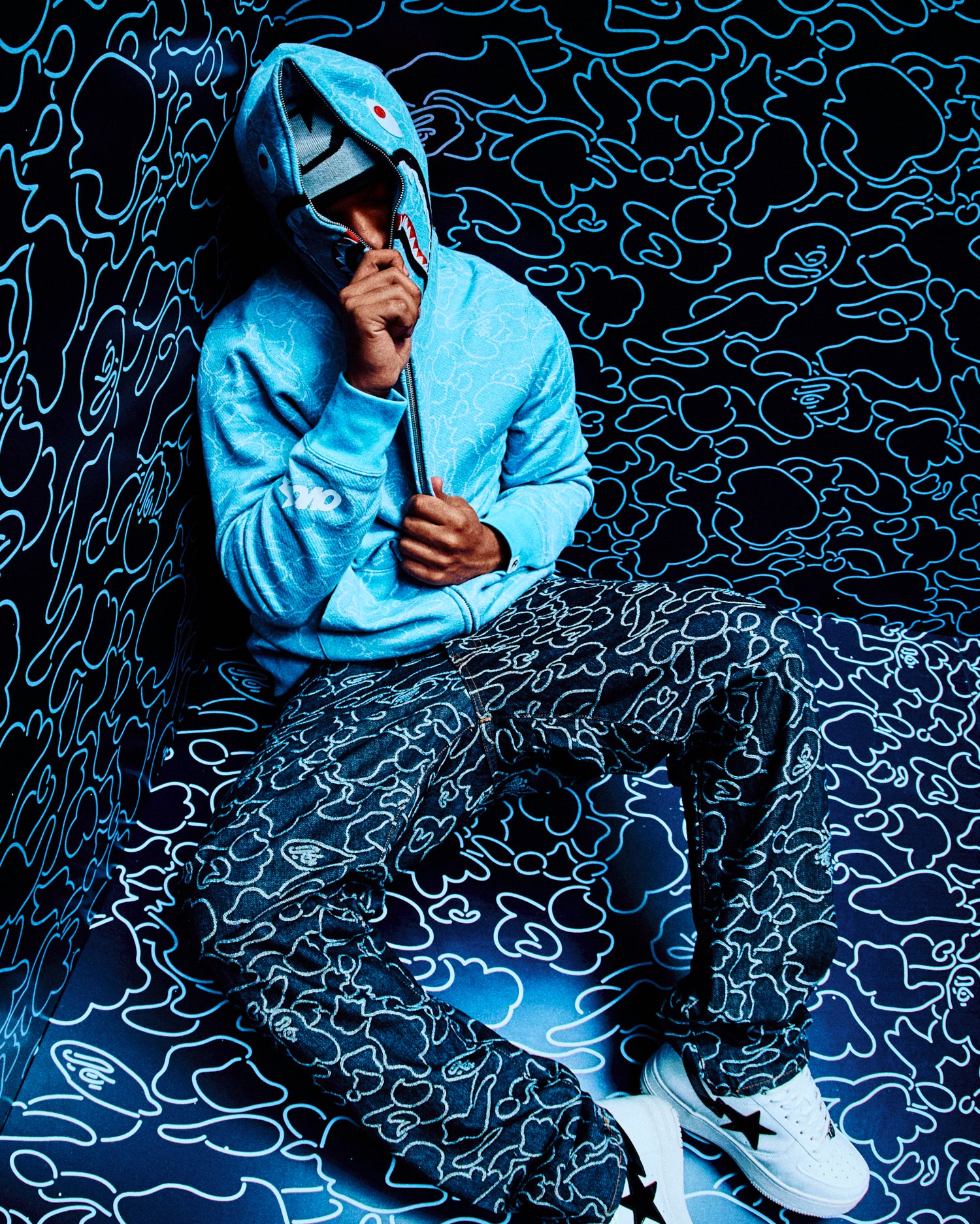Person wearing a October's Very Own x Bape blue hoodie and patterned pants sitting against a matching background