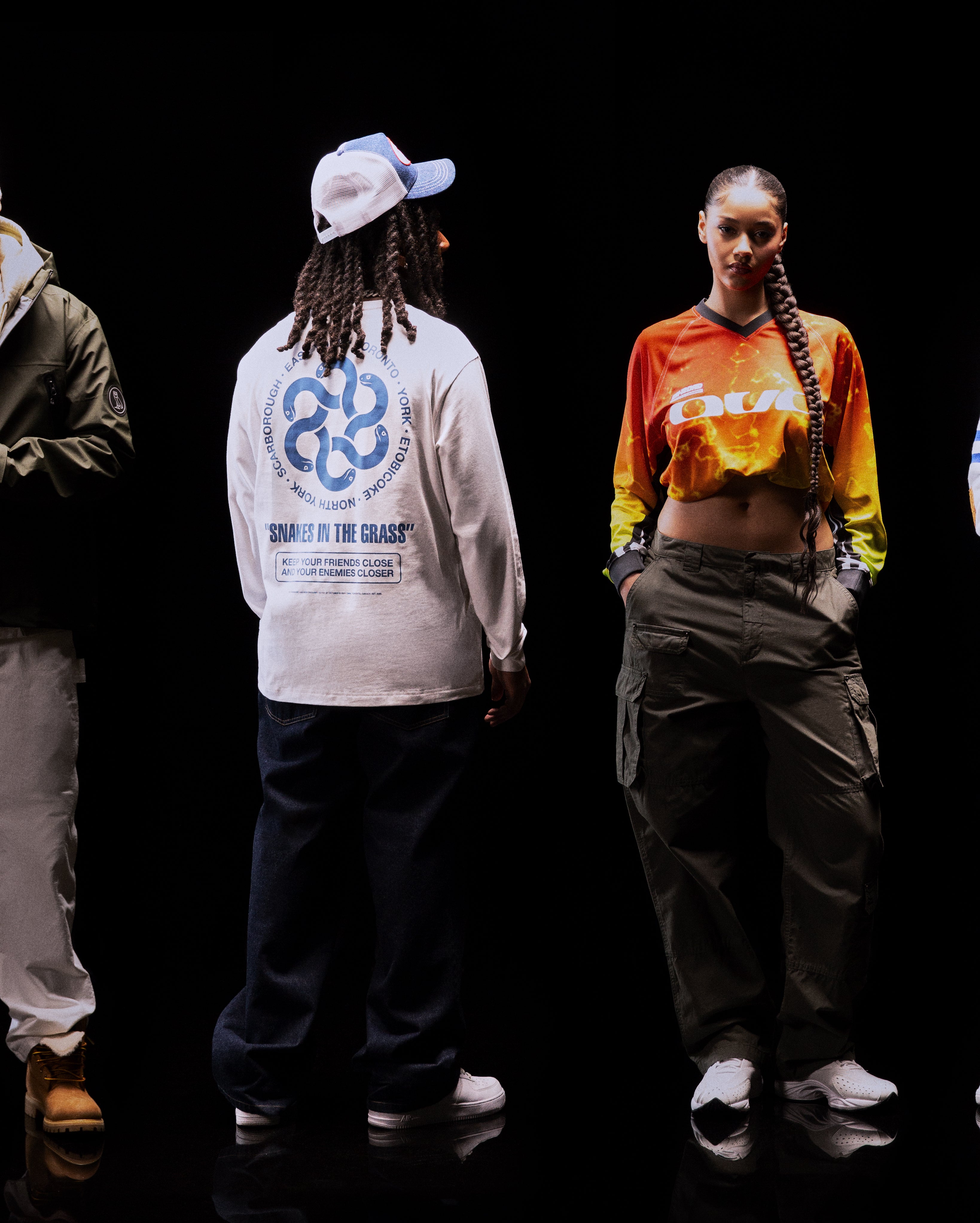 Translation missing: fr.Two people standing on a black background wearing colorful outfits with visible branding