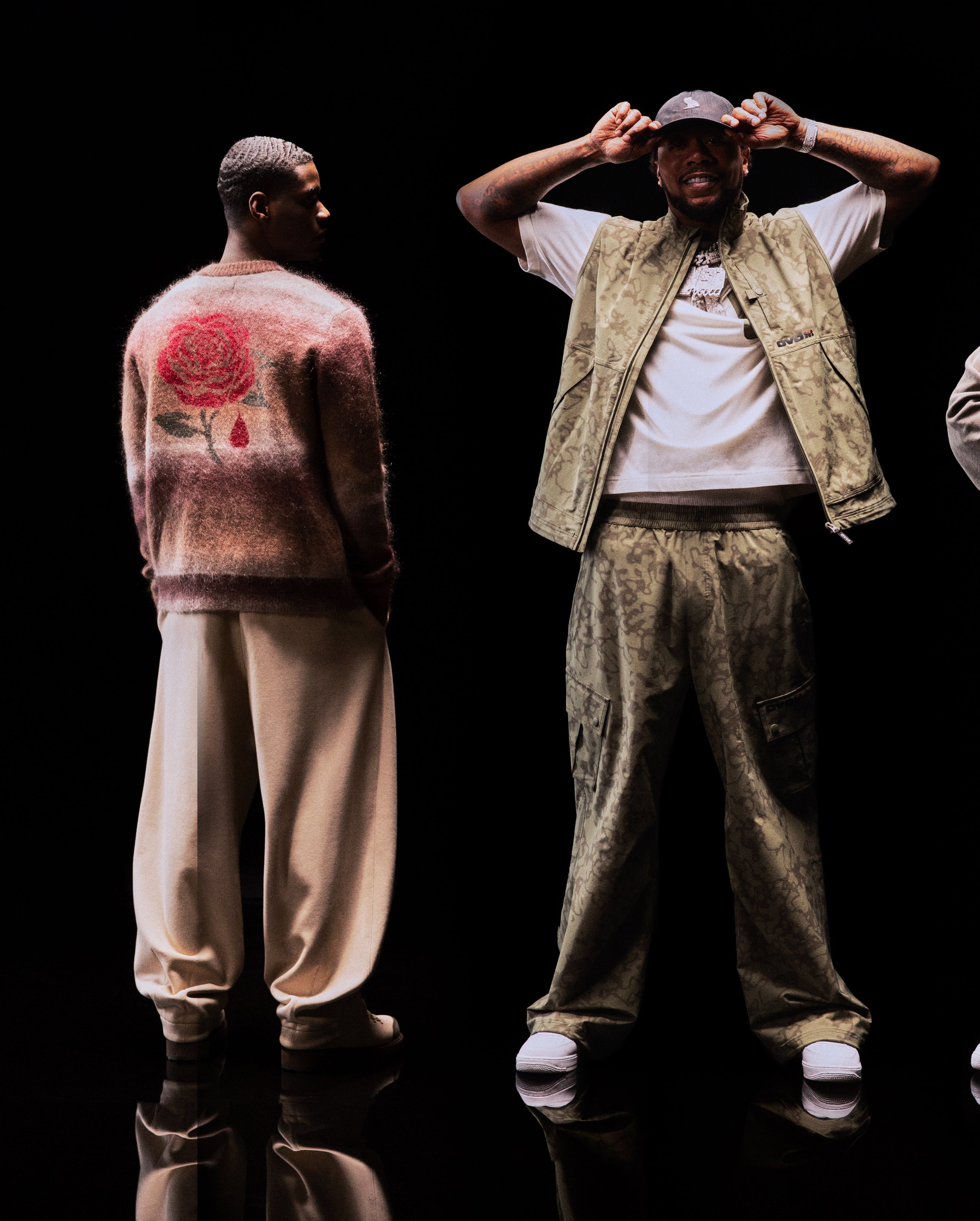 Translation missing: fr.Two individuals standing against a black background, one with a rose design on their sweater