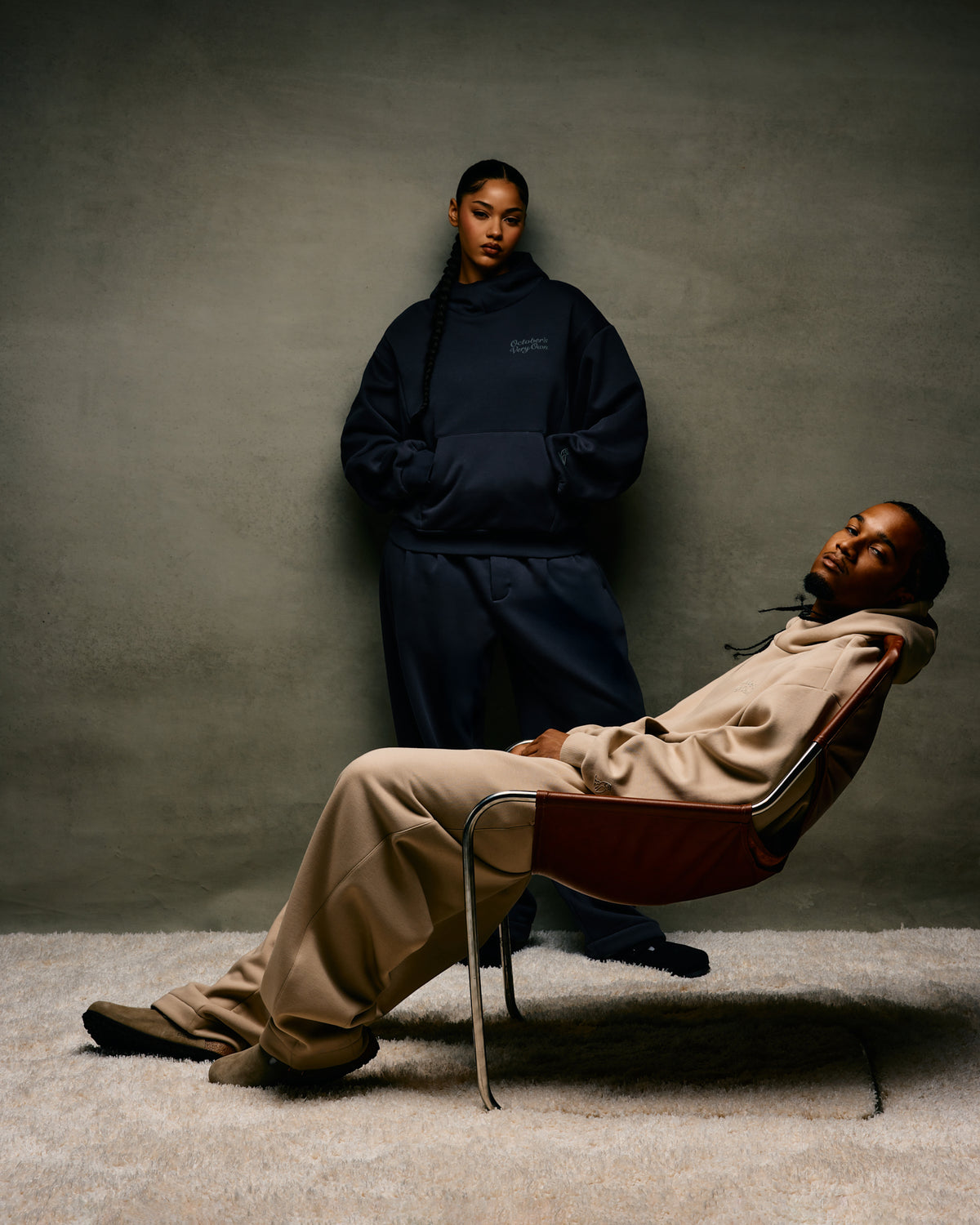 Two people in dark and light-colored October's Very Own outfits against a plain background