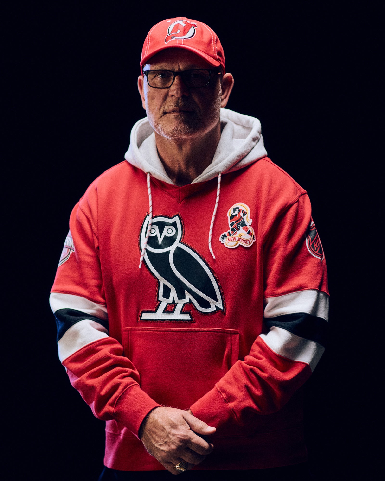 Person wearing a October's Very Own red hoodie with a logo, standing against a black background