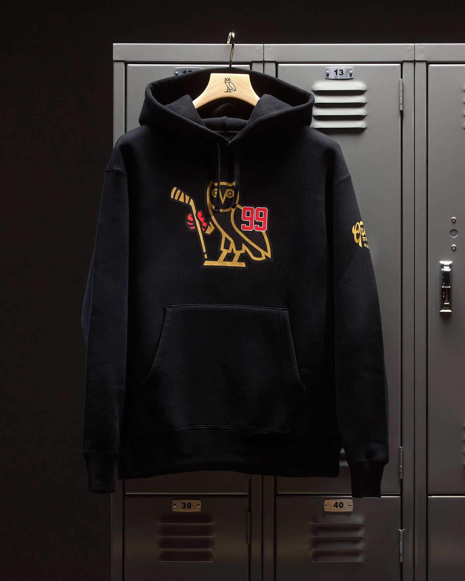 Black Octobers Very Own hoodie with a gold logo hanging on a locker door.