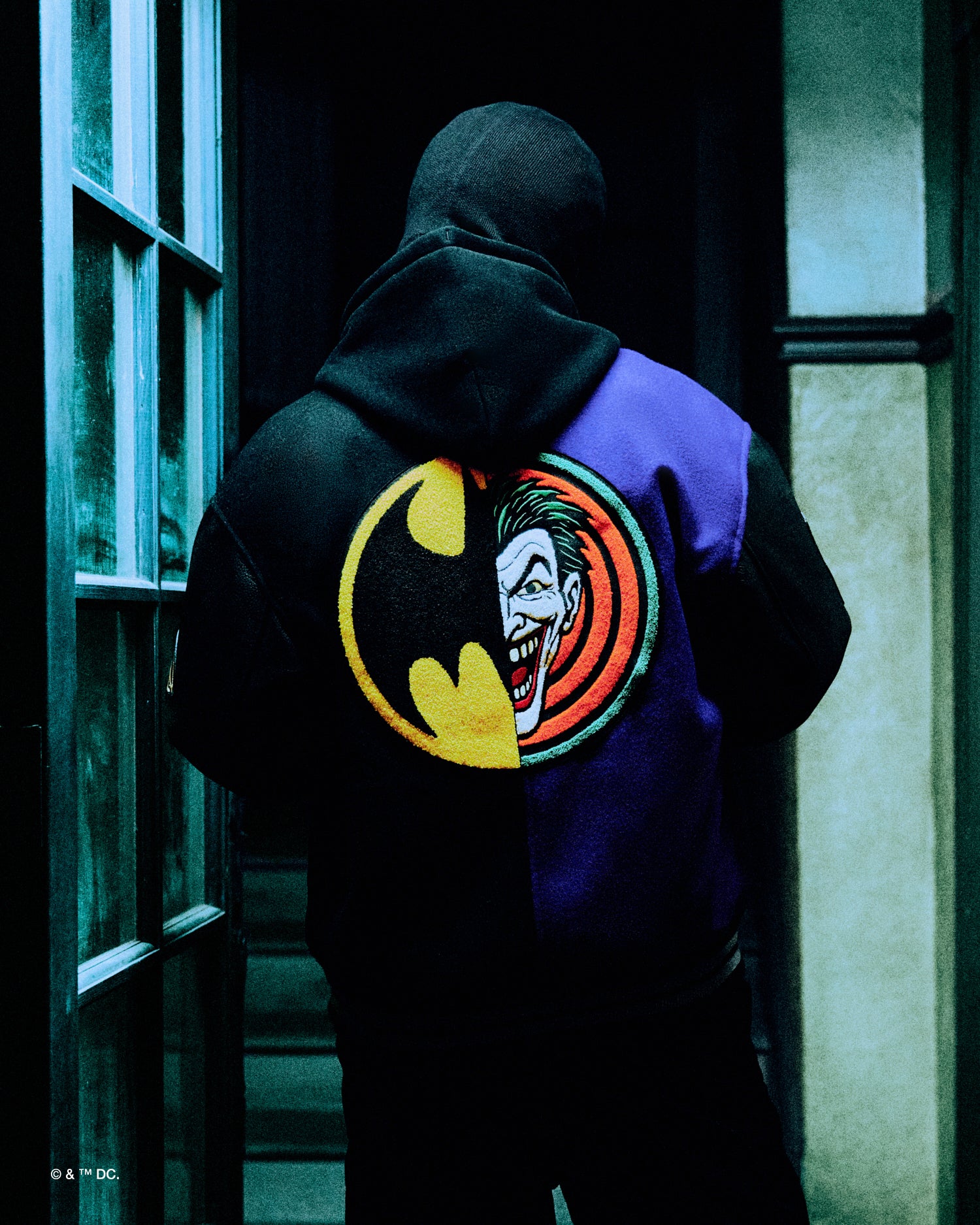 Person wearing a October's very Own x Batman x The Joker hoodie with a colorful logo featuring a face and bat symbol.