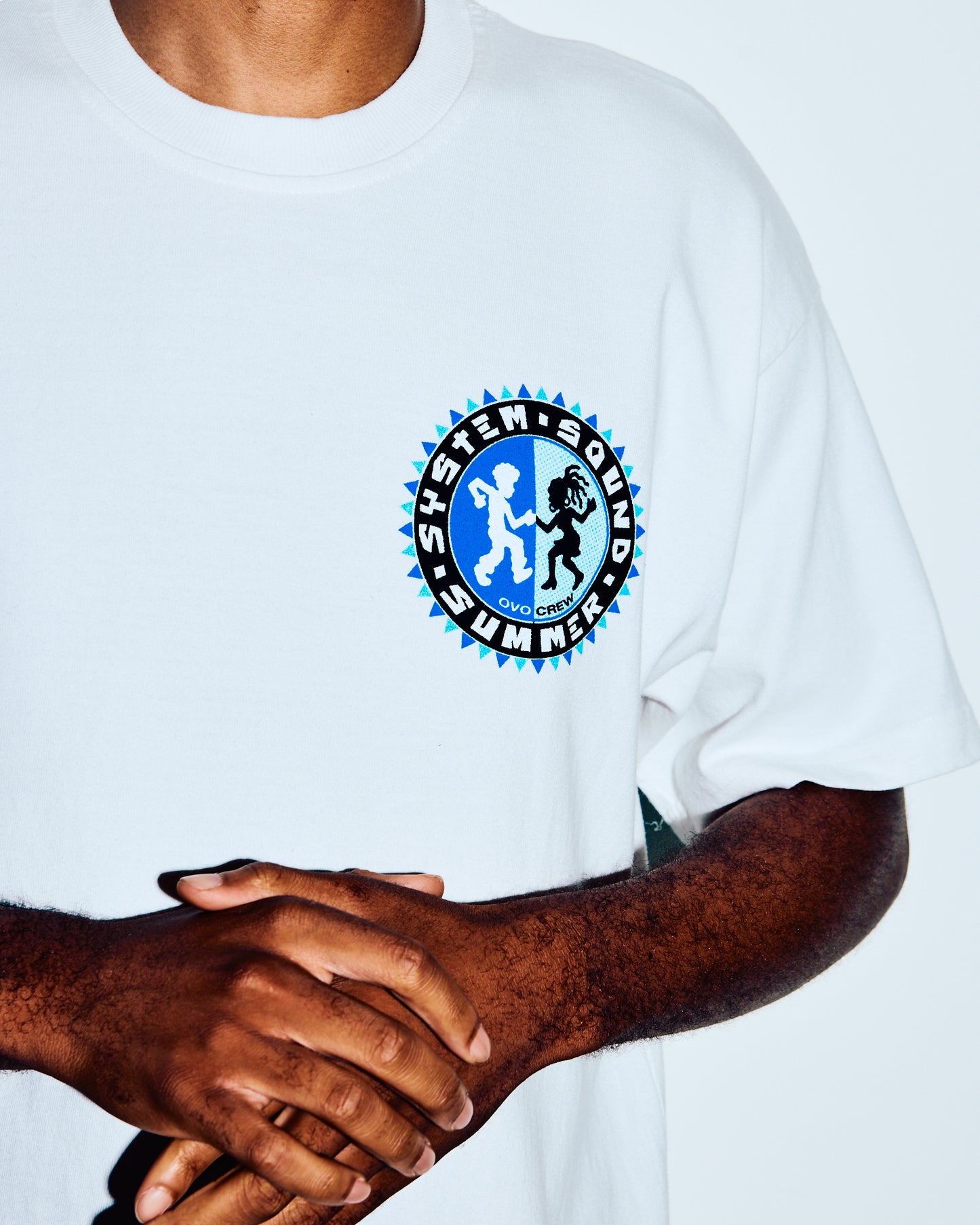 Off-white t-shirt with blue and black circular graphic logo on chest, worn by person with brown skin tone.