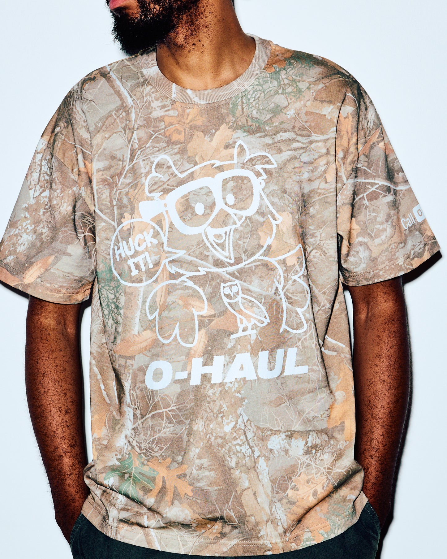 Men's short-sleeve tee in tan and green camouflage print with white graphic and text design.