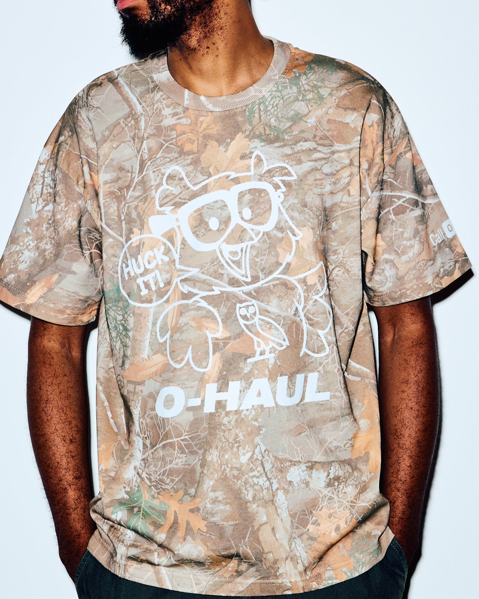 Men's short-sleeve tee in tan and green camouflage print with white graphic and text design.