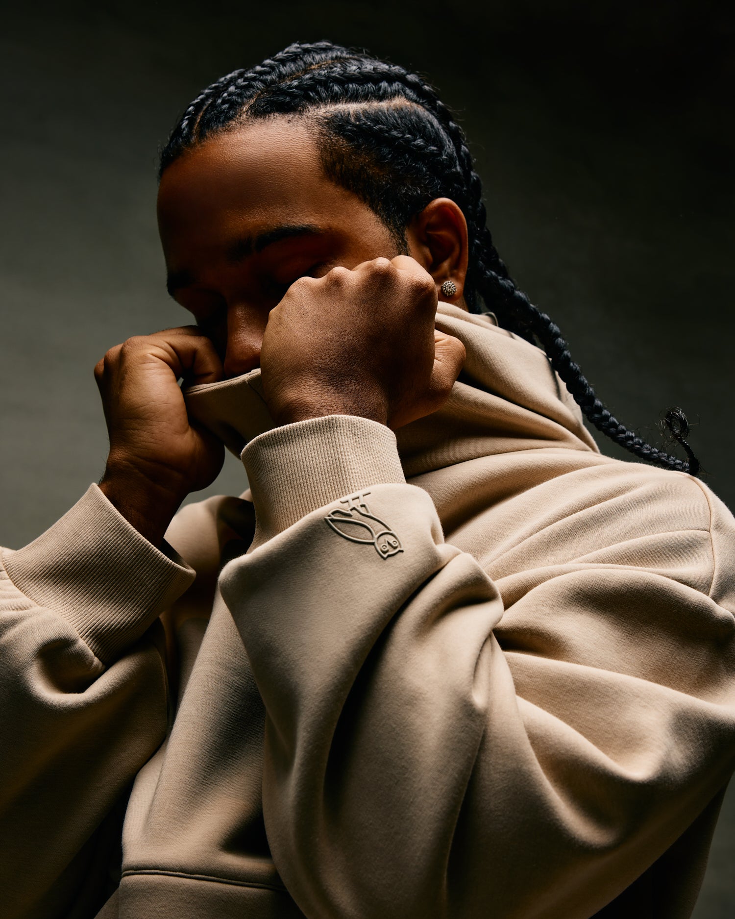 Person wearing a beige October's Very Own hoodie with a brand logo, sitting against a dark background