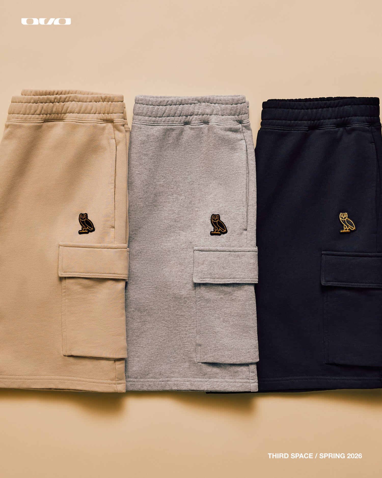 Three pairs of sweatpants in beige, gray, and navy with a logo on a beige background.