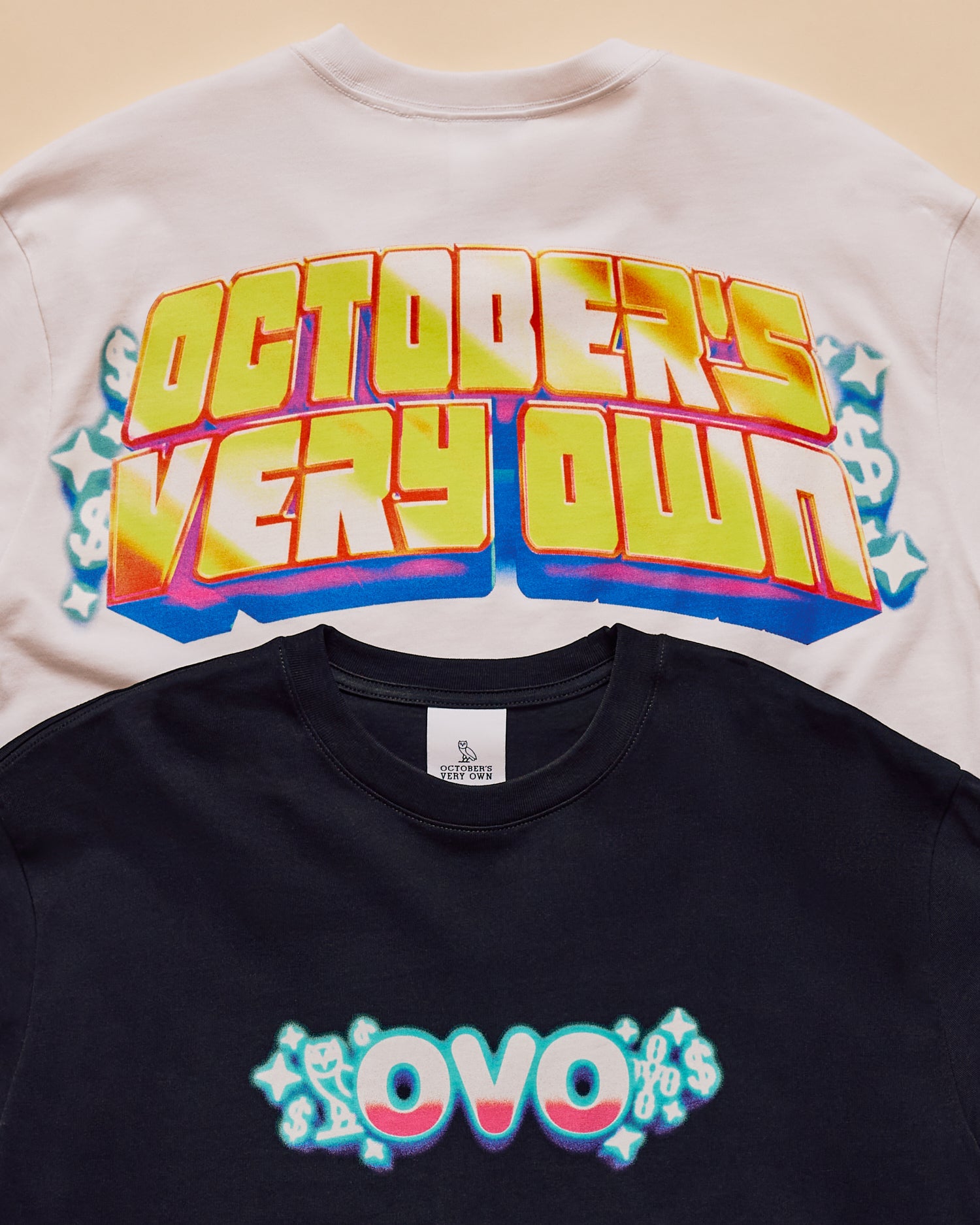 Two October's Very Own t-shirts with colorful text designs on a beige background