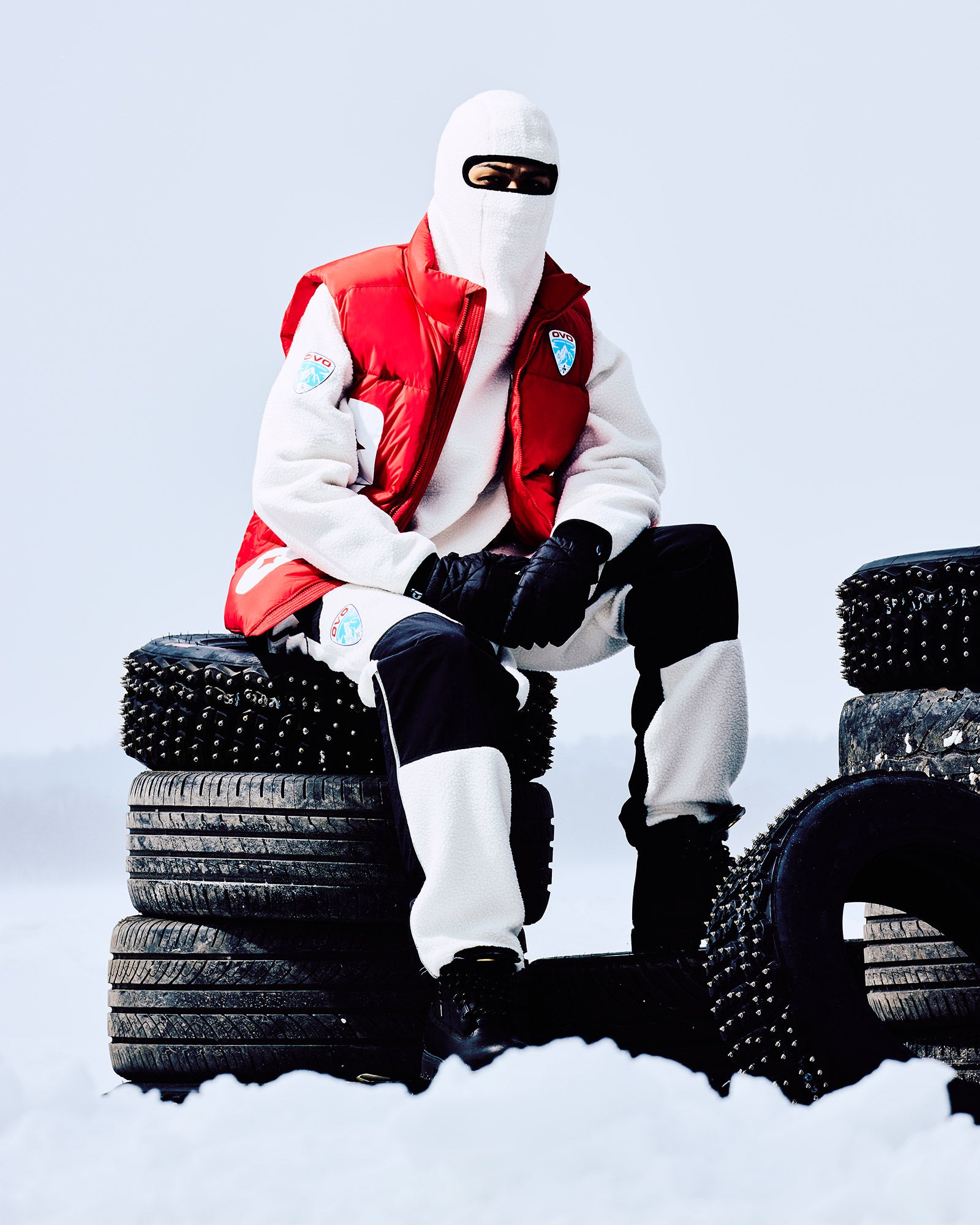 Person in winter October's Very Own gear sitting on a stack of tires in the snow