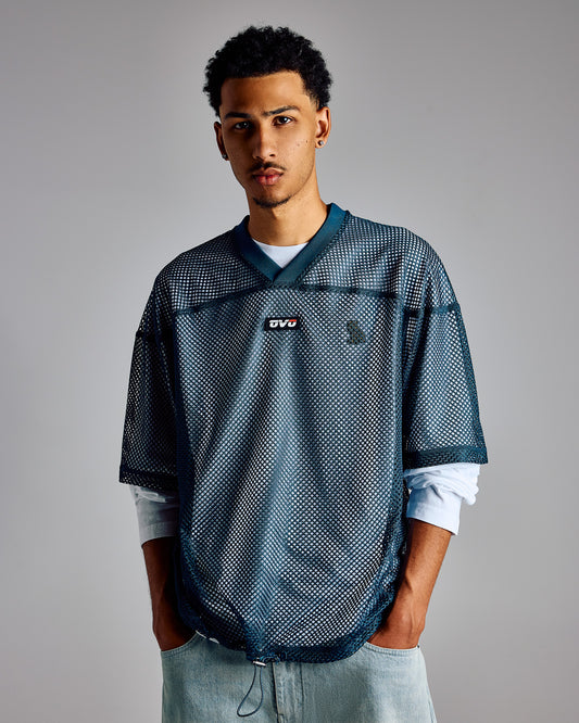 Teal mesh football jersey with dark navy panels, small logo at chest, worn over white long-sleeve shirt.