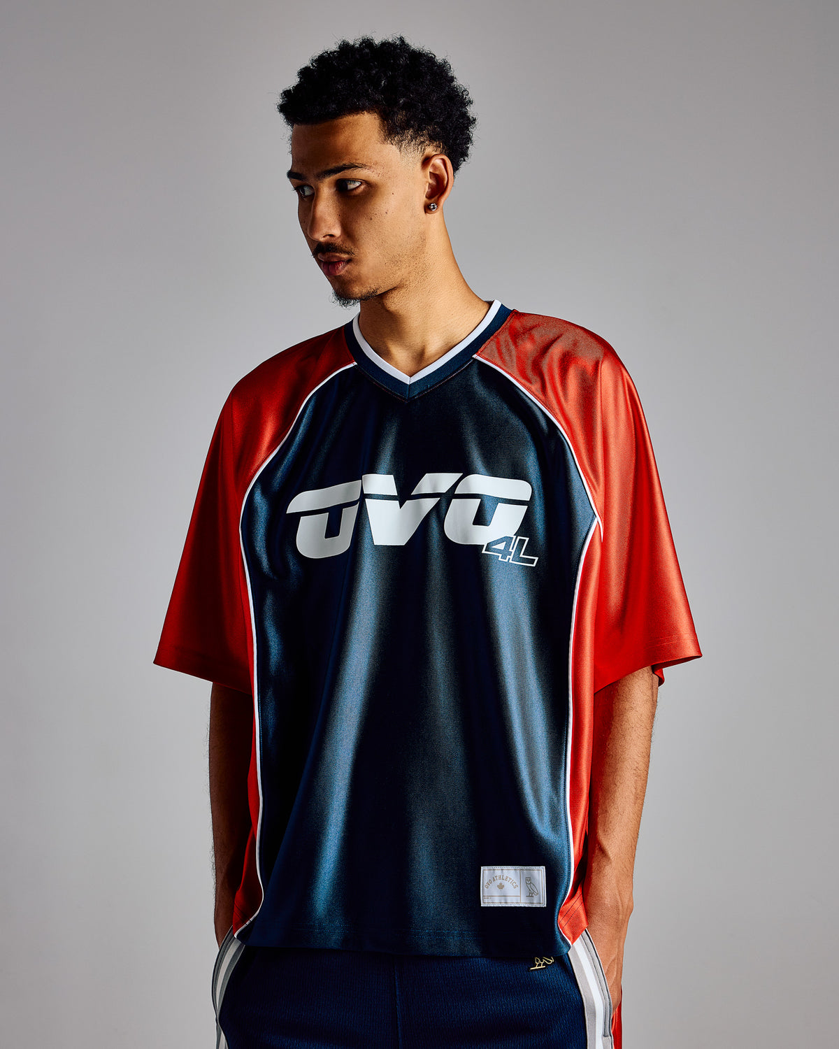 Midnight green and red colorblock athletic jersey with white logo graphic and V-neckline.