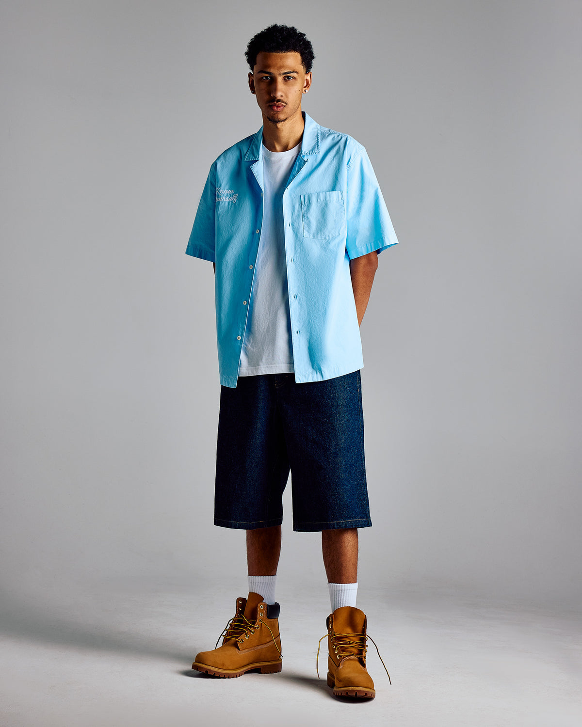 Two-tone camp shirt in light blue and navy with chest pocket, worn over white tee with navy shorts.