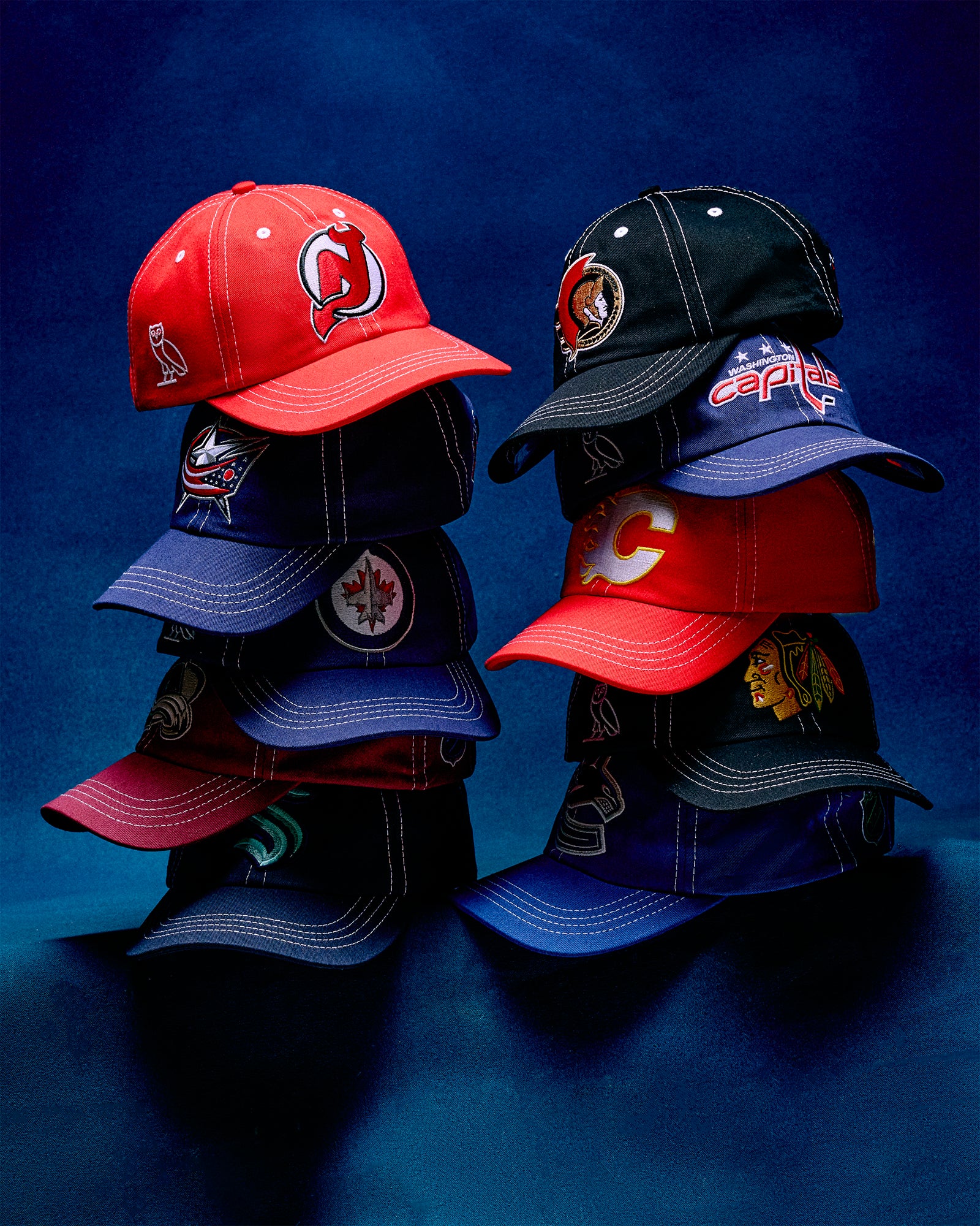 Stack of various October's Very Own x NHL baseball caps on a blue background