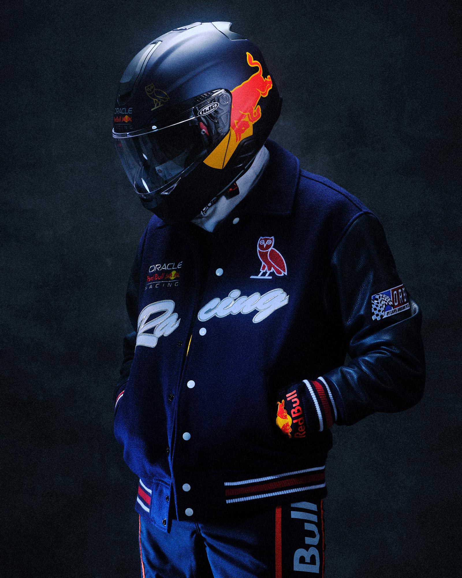 Man wearing Red Bull Racing Helmet wearing October's Very Own x Red Bull Racing Varsity jacket