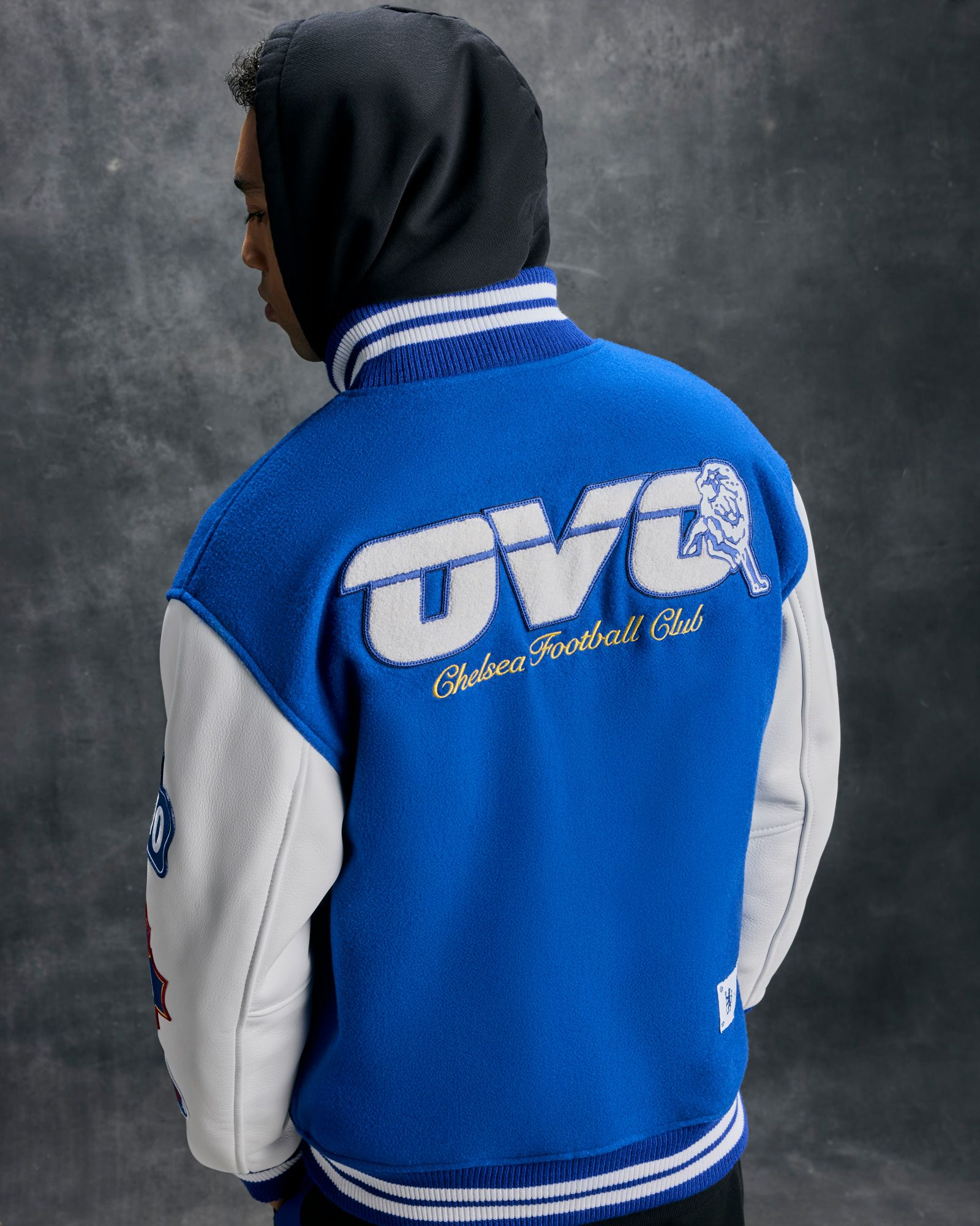 Person wearing a blue and white October's Very Own x Chelsea FC jacket with 'OVO' branding on a gray background
