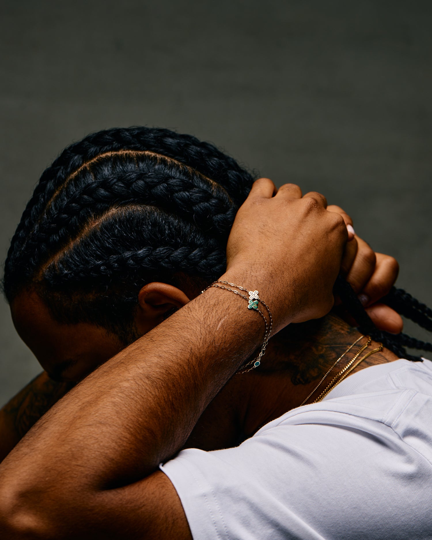 Person with braided hair holding their head, wearing a October's Very Own bracelet with a green stone.