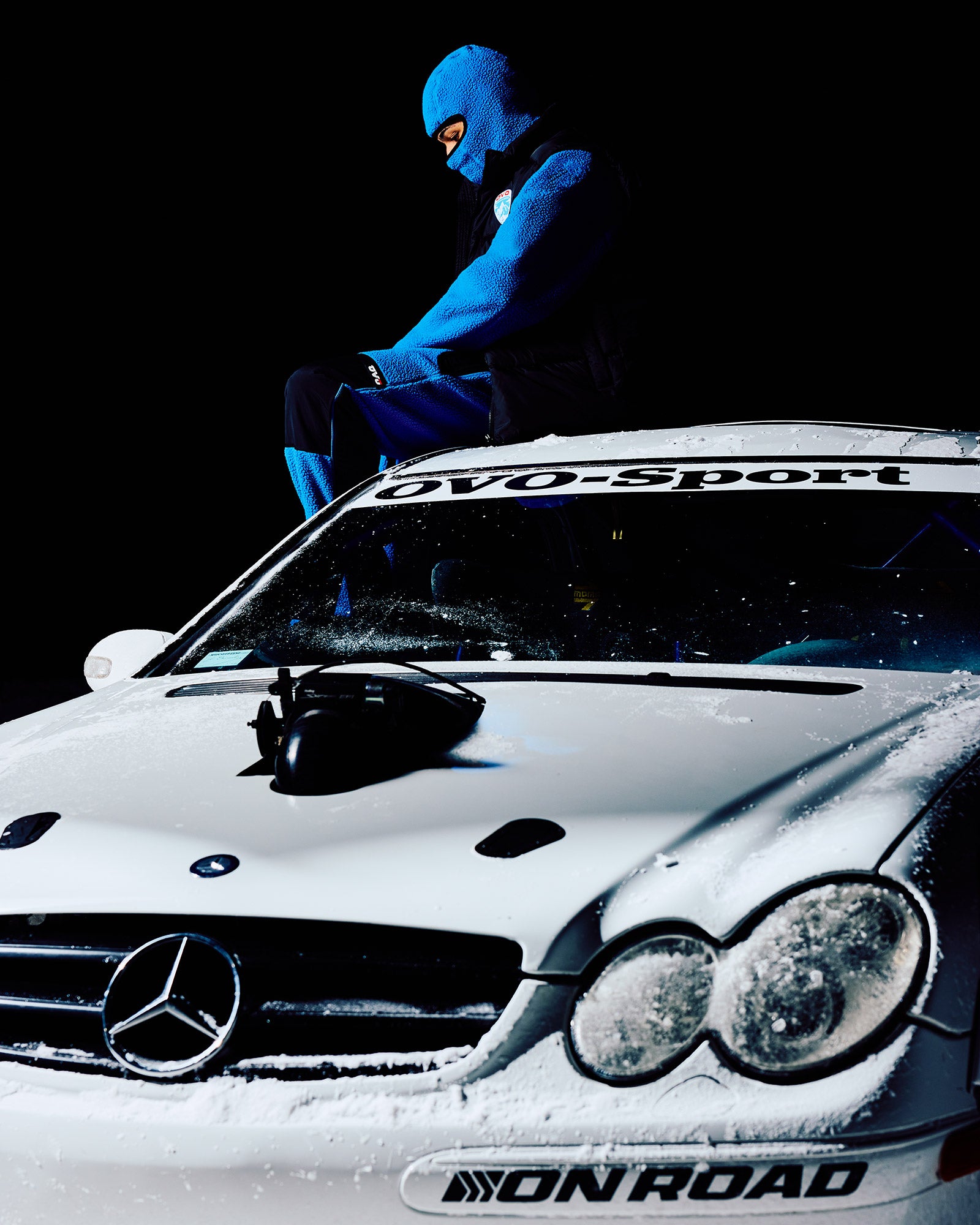 Person in a blue suit sitting on a Mercedes-Benz car with 'DVO-Sport' branding.