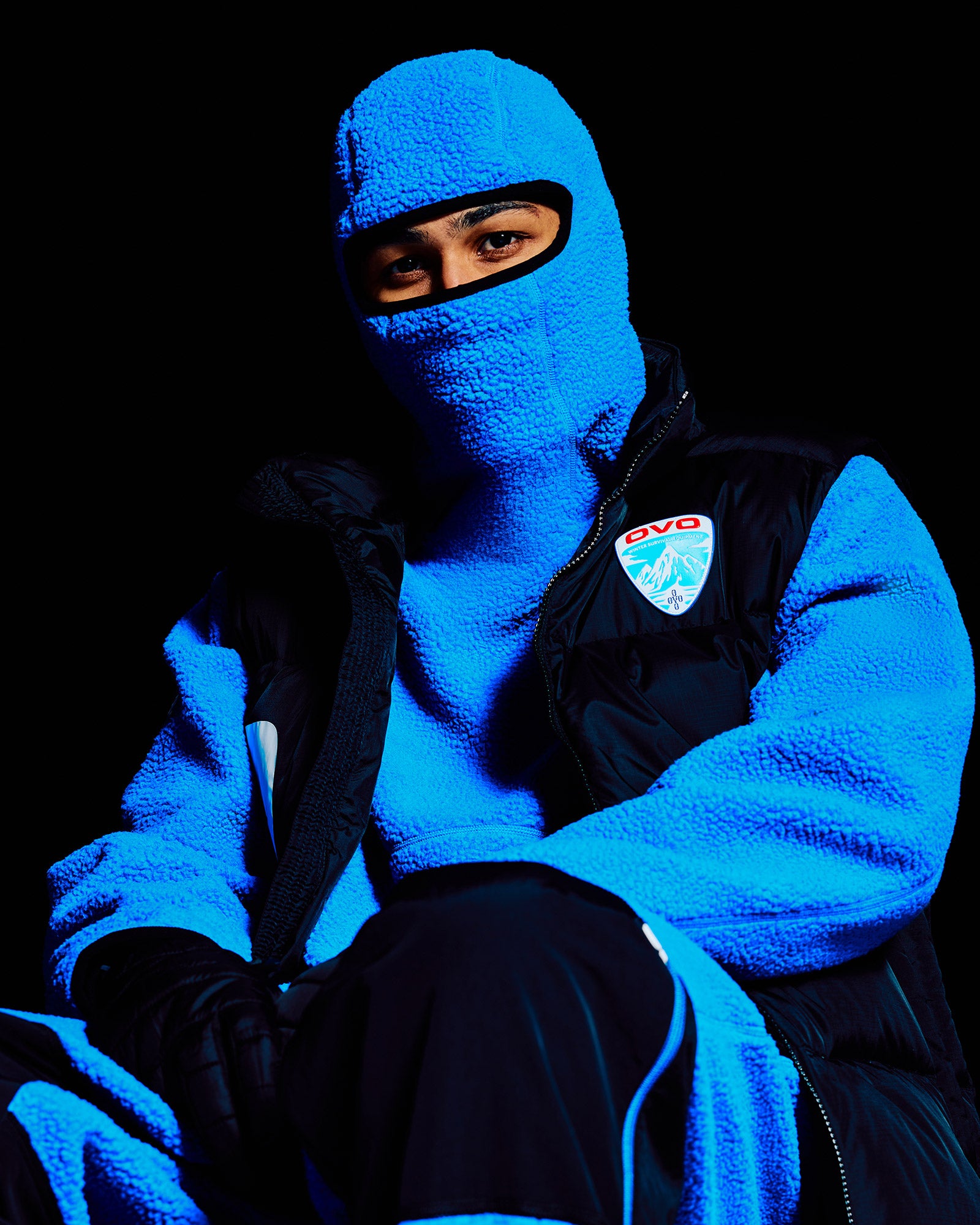 Person wearing a blue October's Very Own balaclava and black jacket with a logo on a black background