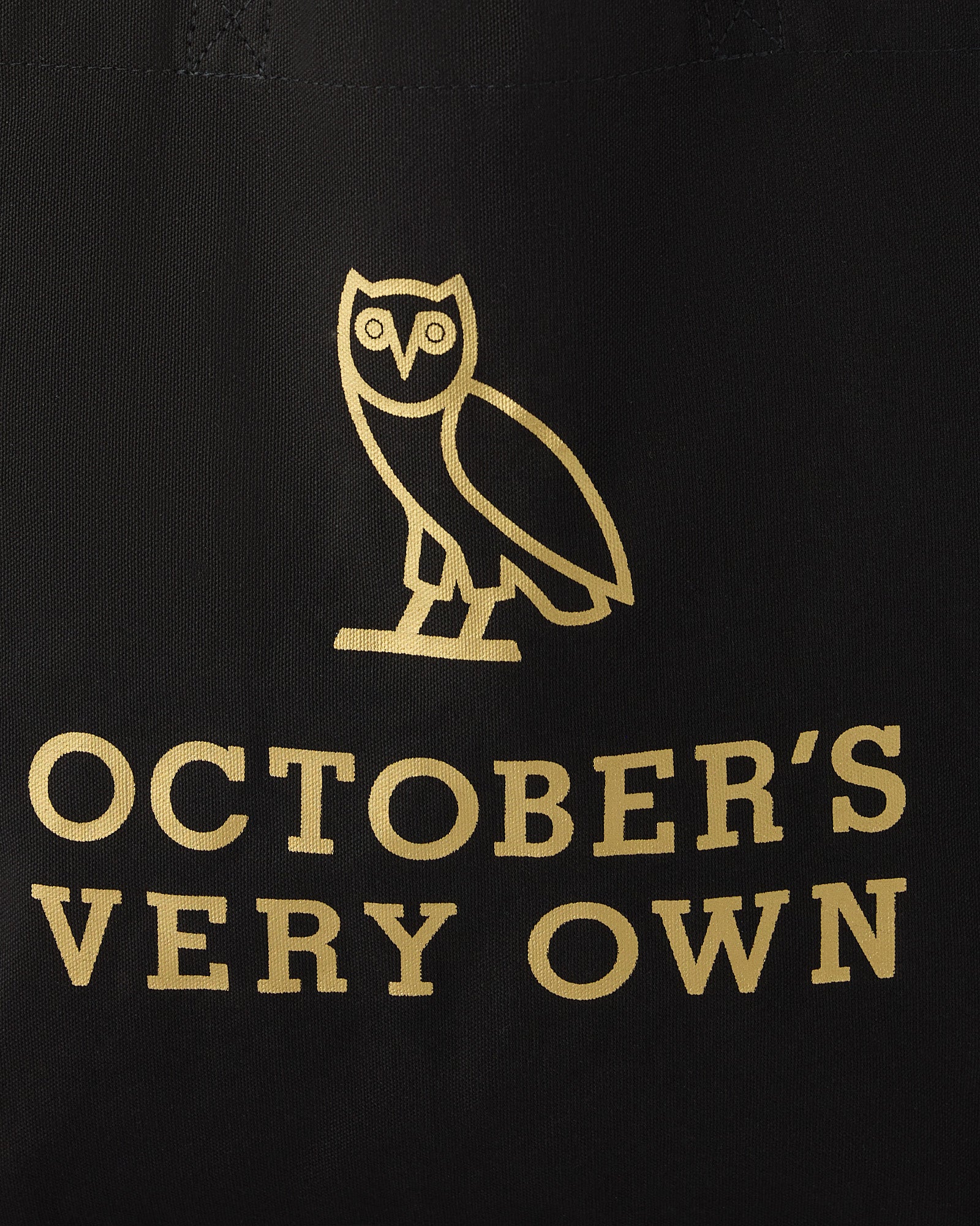 Black tote bag with gold owl graphic and "October's Very Own" text printed on front.