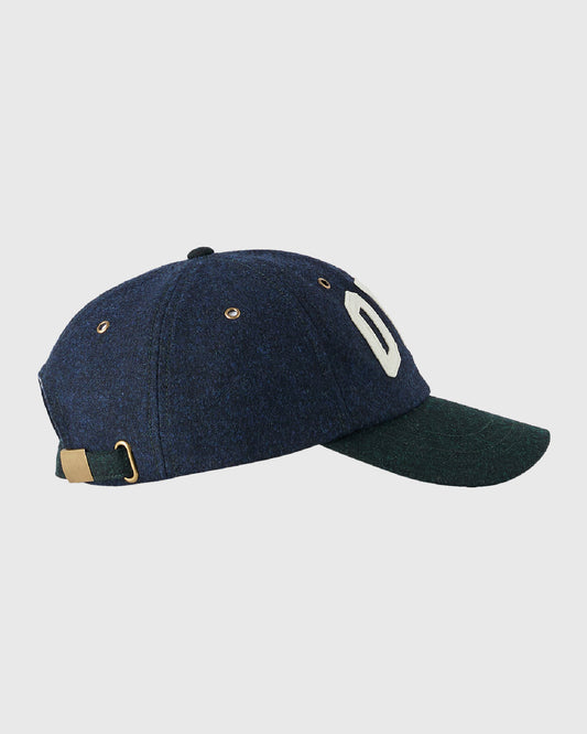 Navy wool cap with green visor, white curved logo on side, tan back strap, and metal eyelets.