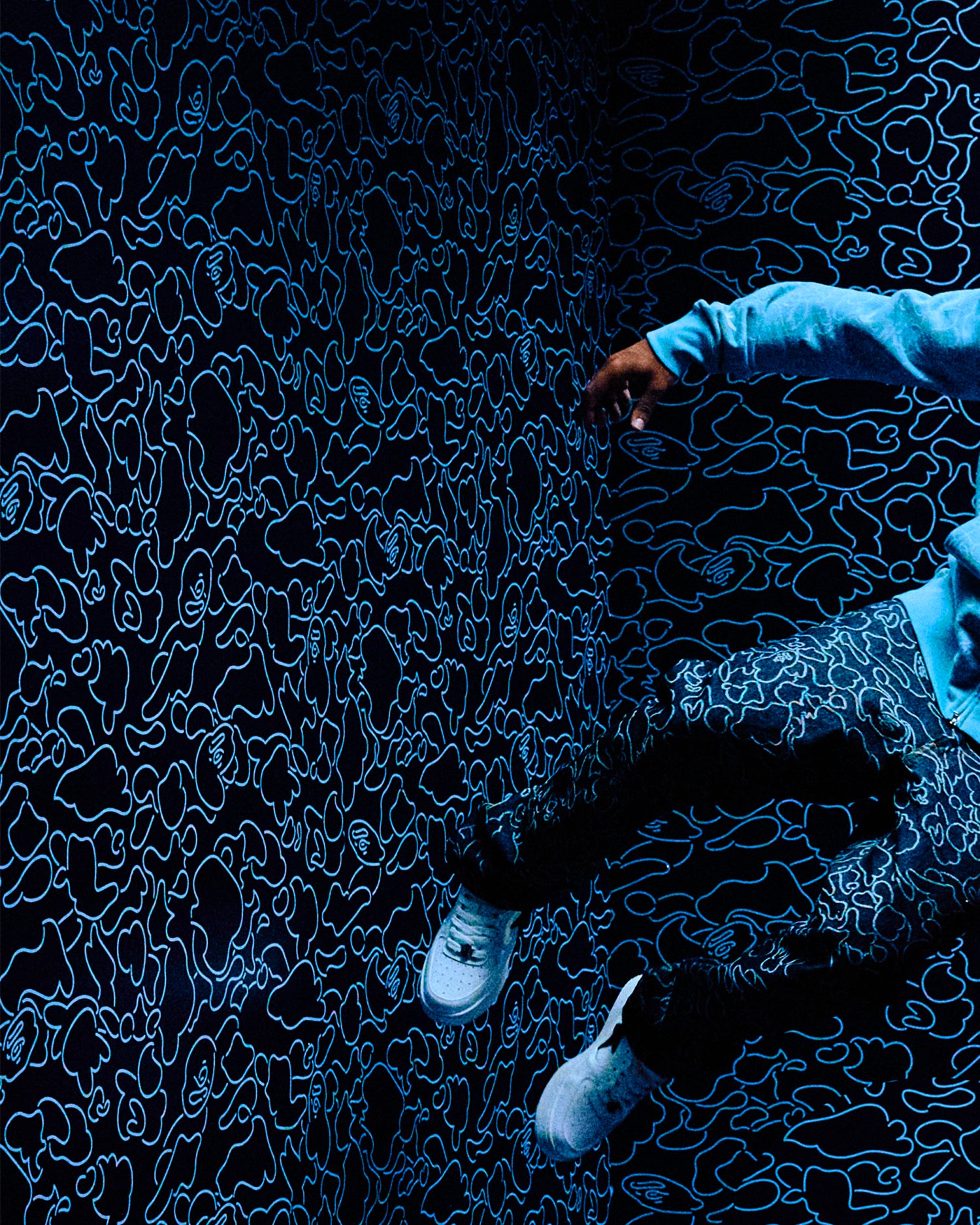 Person wearing a blue patterned Octobers Very Own x Bape outfit interacting with a dark textured surface