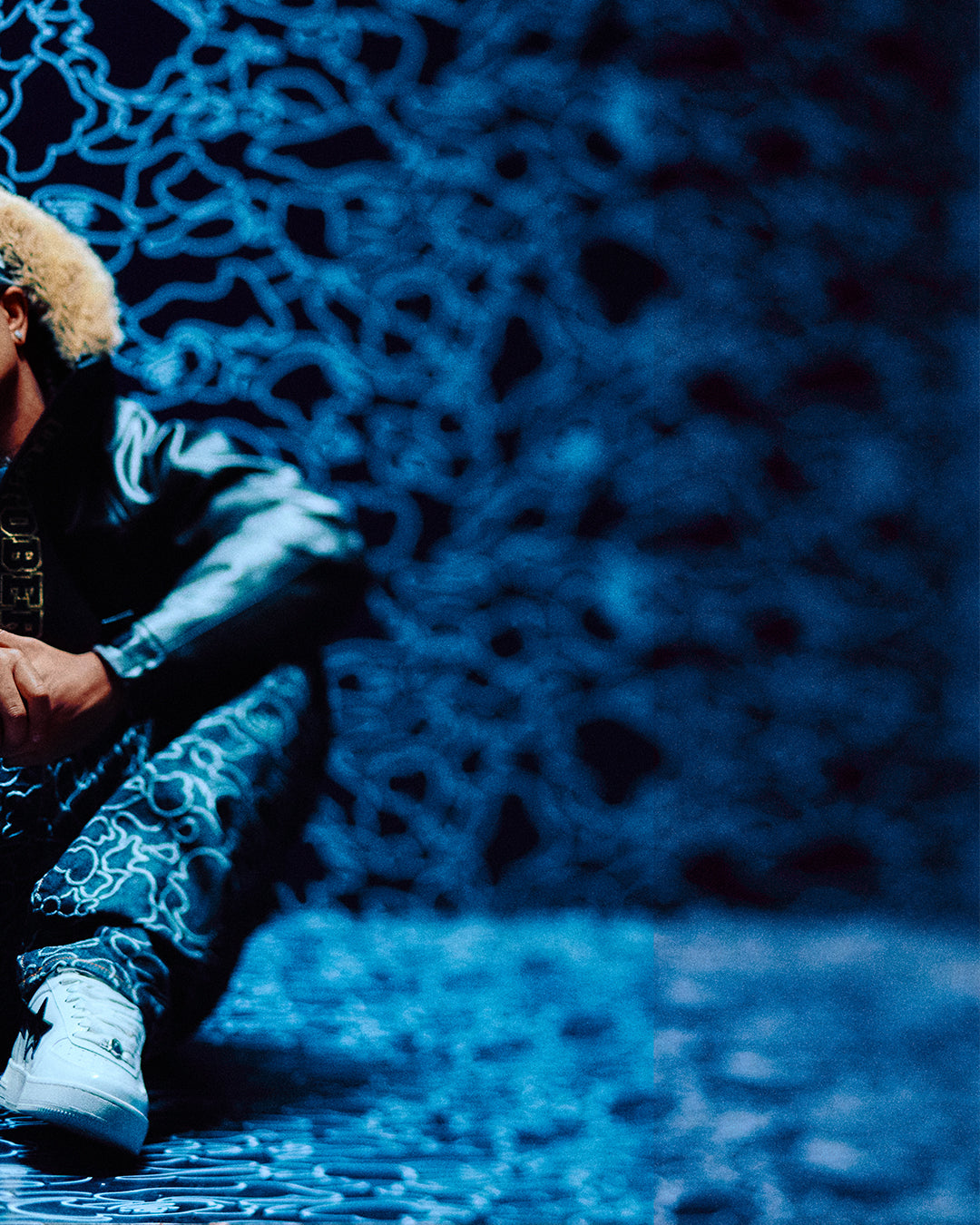 Person wearing October's Very Own x Bape fur-lined coat and hat against a dark, textured wall with abstract patterns.