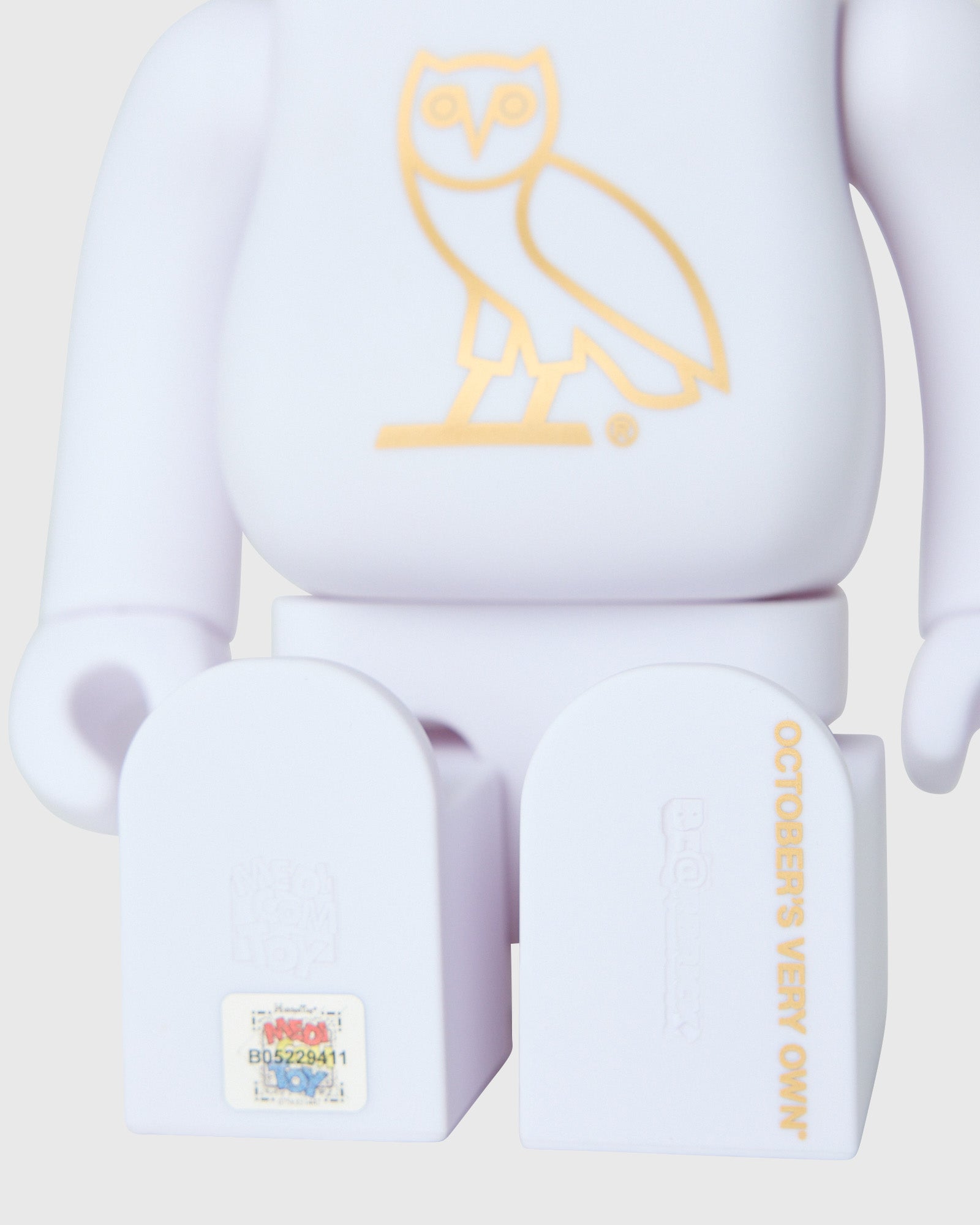 Pearl white BE@RBRICK figure with gold owl design on chest, shown from front with visible feet and branding details.