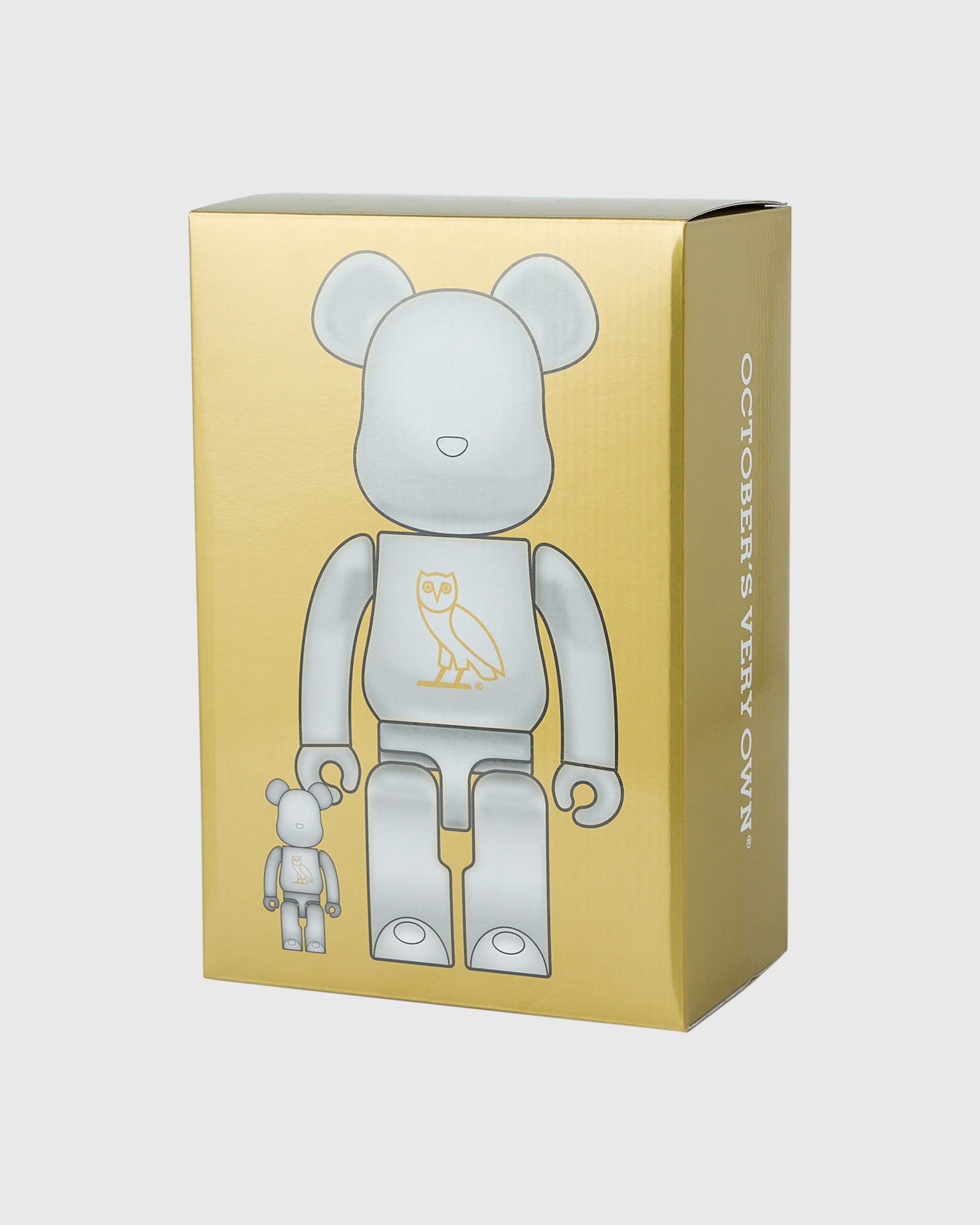 Pearl white BE@RBRICK figures in two sizes with owl chest design displayed in gold packaging box.
