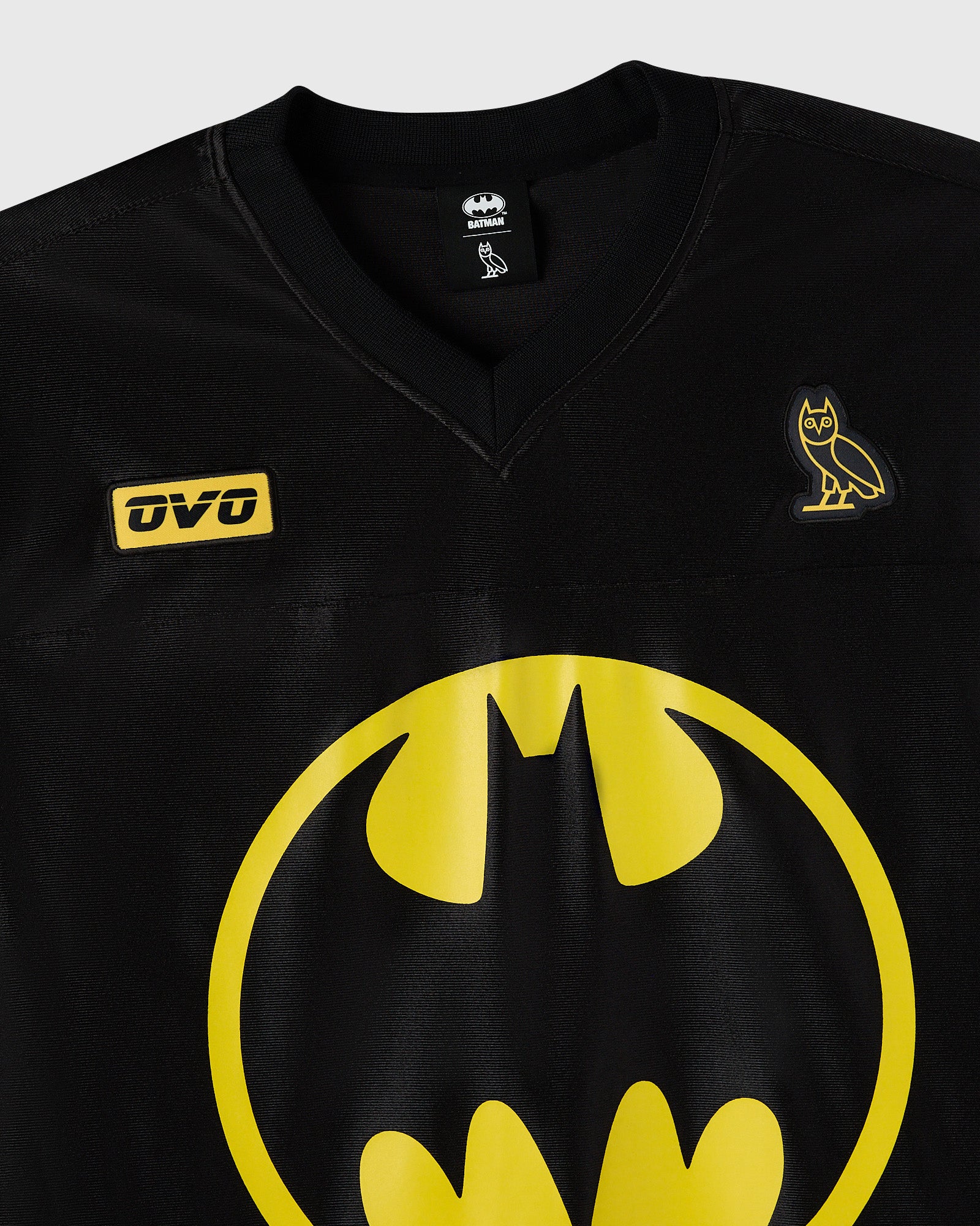 Black v-neck football jersey with yellow Batman logo, OVO sponsor patch, and owl emblem on chest.