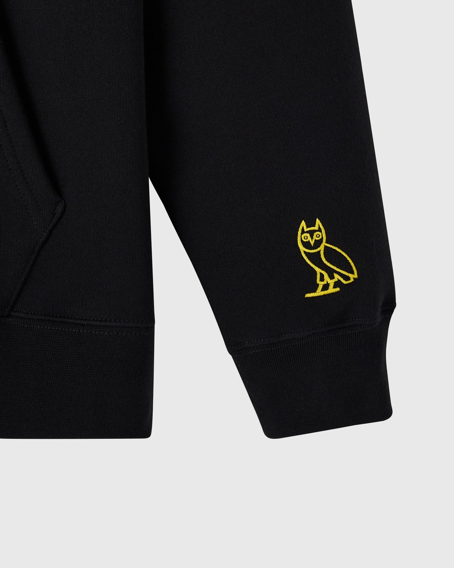 Black hoodie sleeve with yellow owl embroidery on cuff.