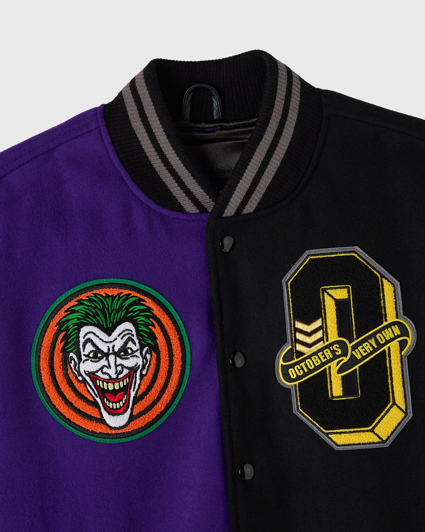 Black and purple varsity jacket with embroidered Joker face on left side and Batman shield on right side, striped ribbed coll