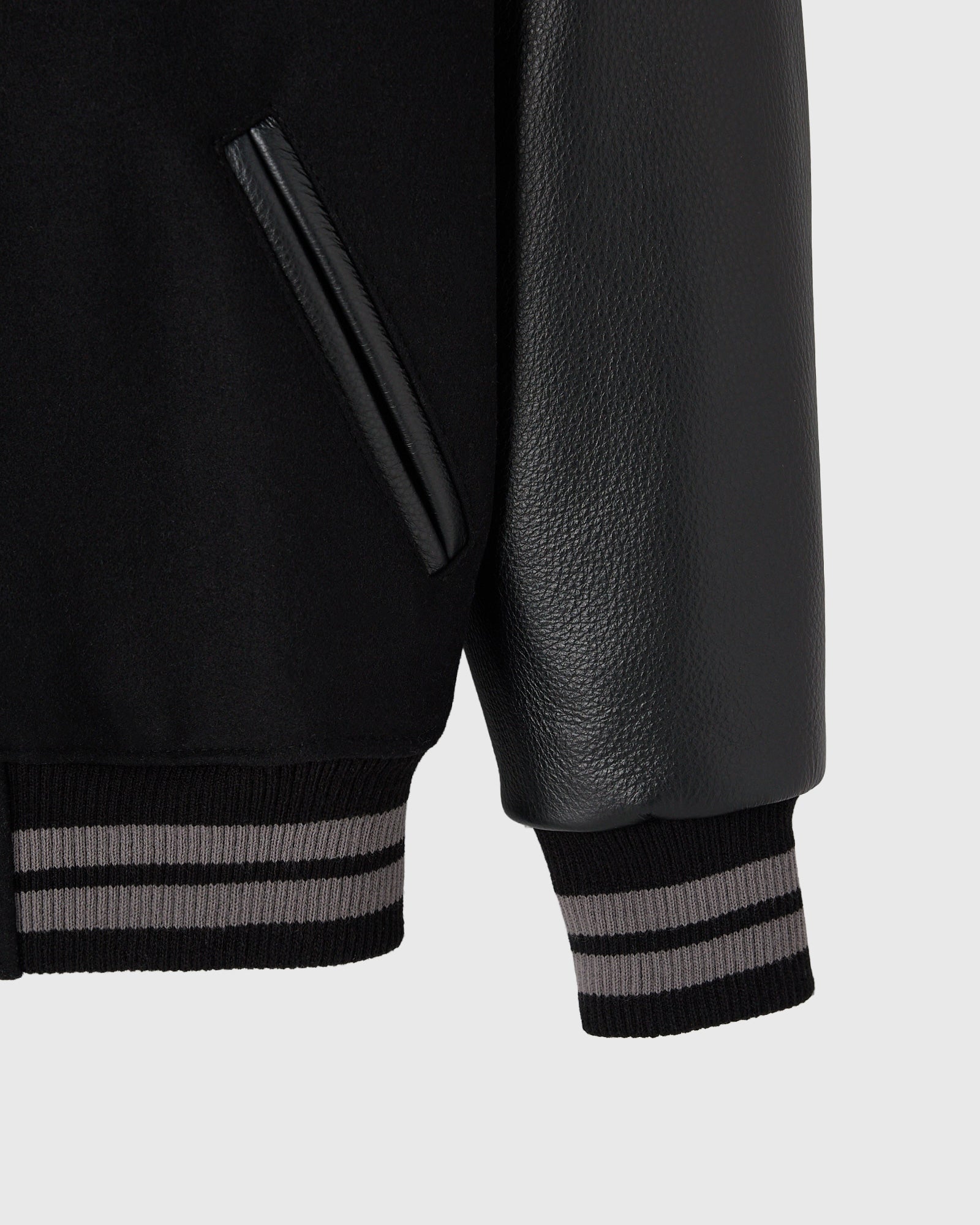 Black varsity jacket with textured leather sleeves, striped ribbed cuffs, and chest pocket detail.