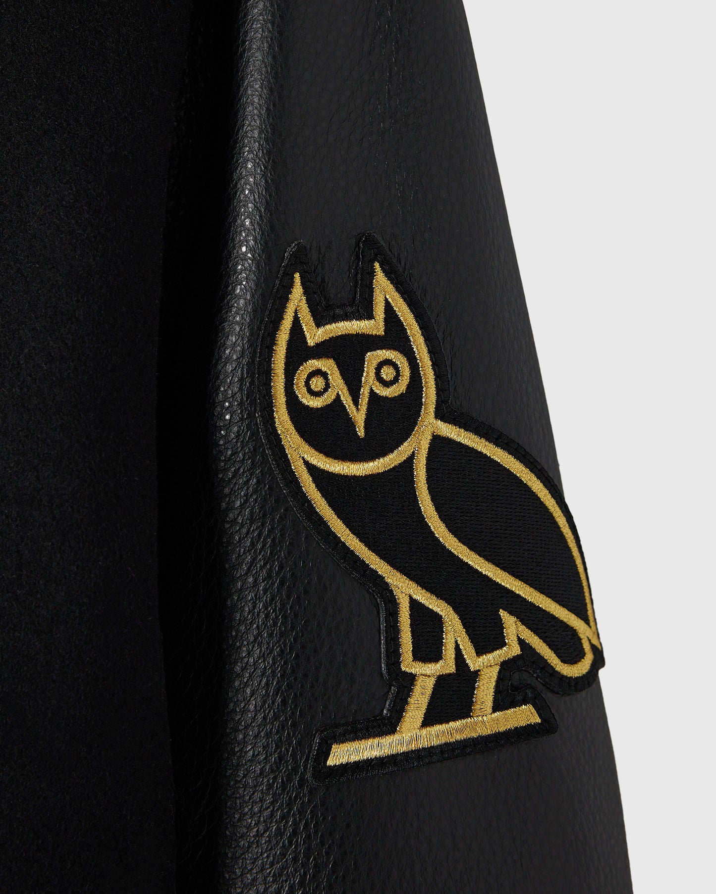Black varsity jacket with gold-embroidered owl patch on sleeve.