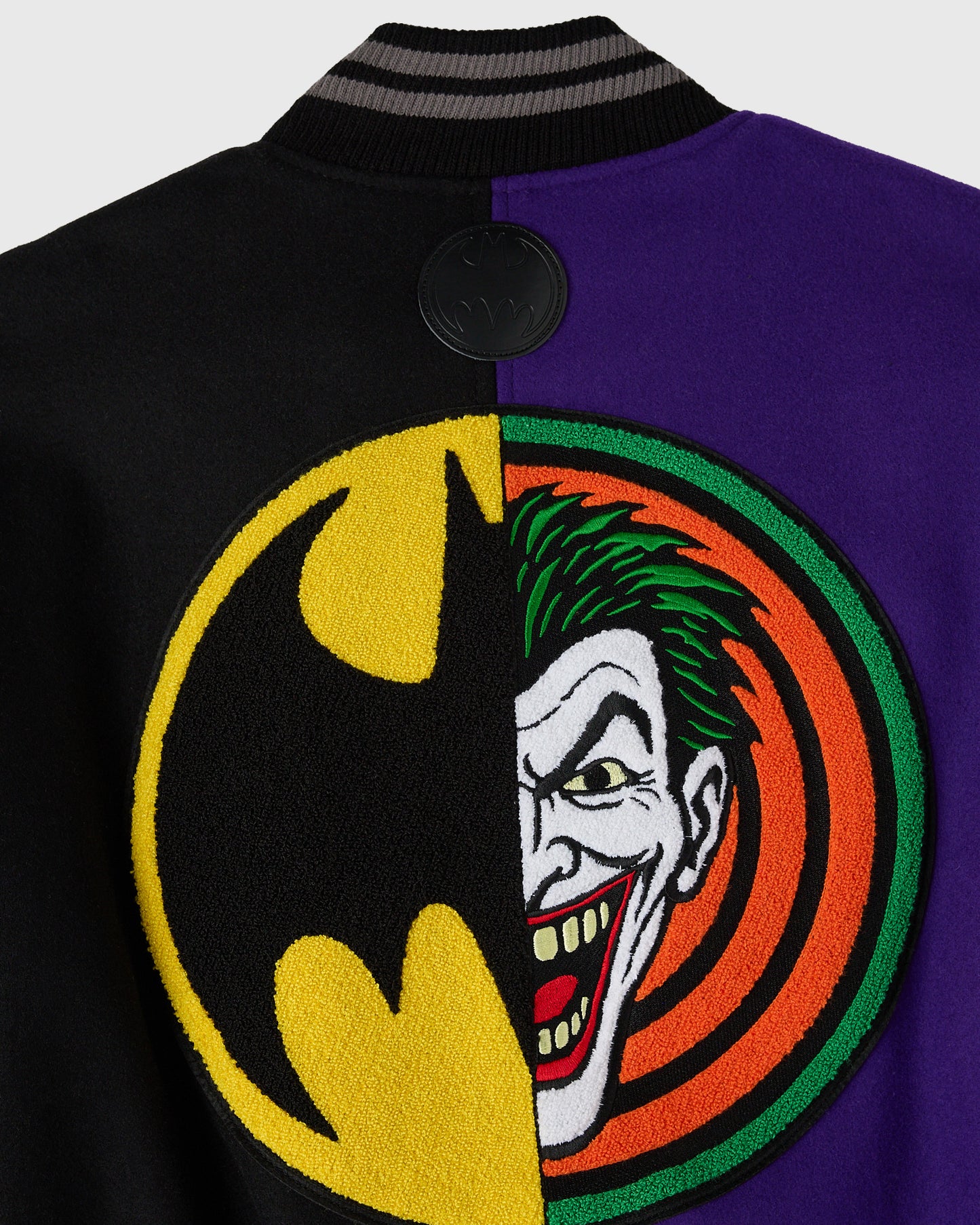Black and purple varsity jacket with split Batman and Joker circular emblem on chest and black button.