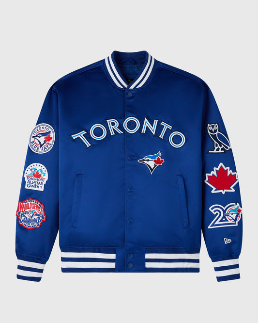 Blue varsity jacket with Toronto Blue Jays branding, white striped ribbing at collar and cuffs, and multiple team logos on sl