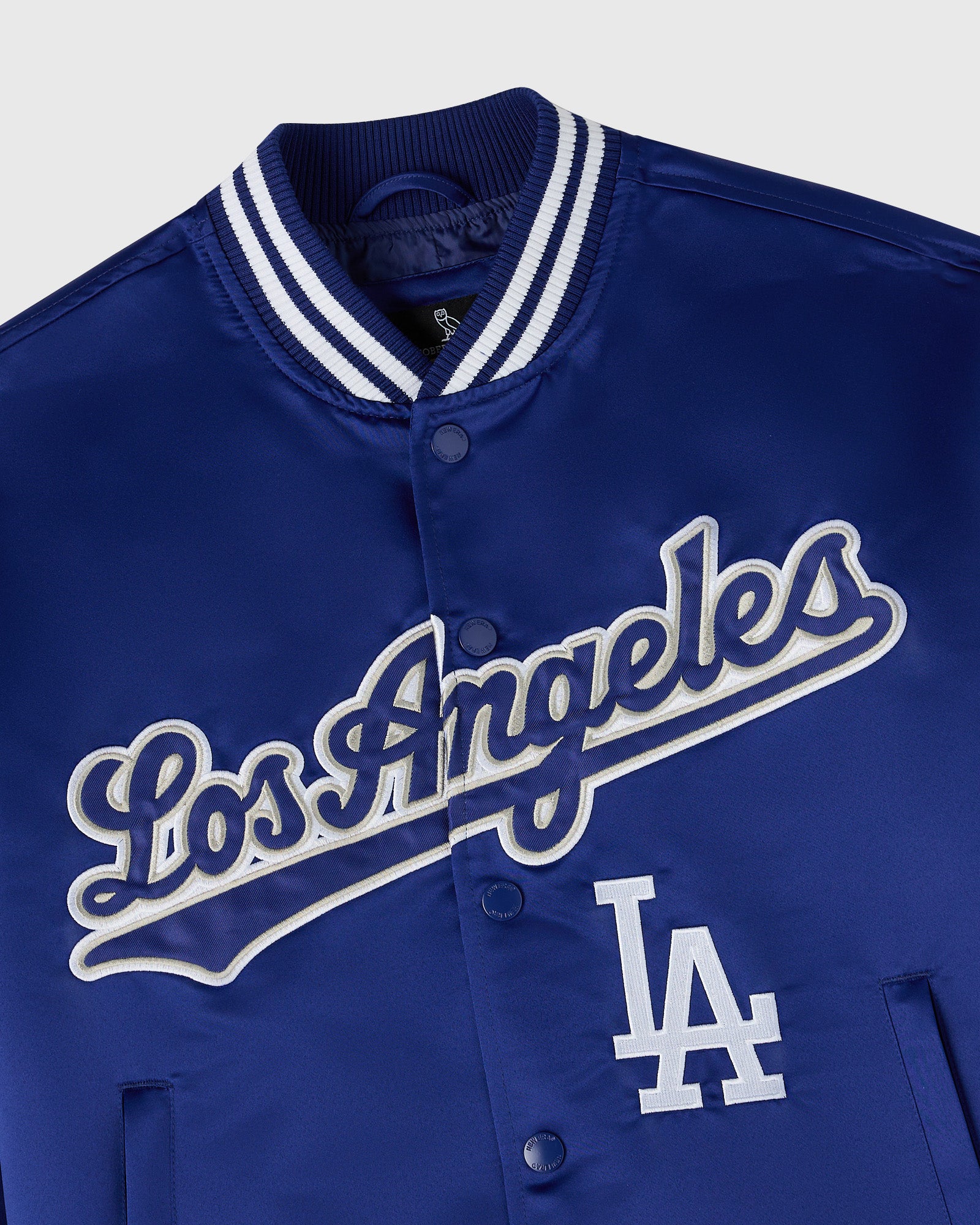 Royal blue varsity jacket with "Los Angeles" script and "LA" logo in white, white striped ribbed collar, and snap button fron