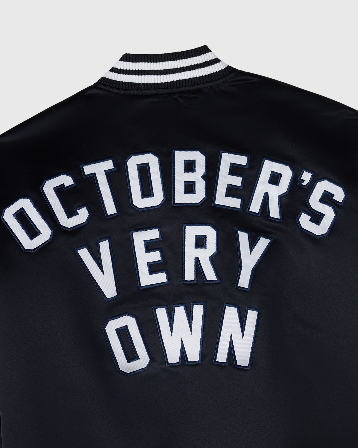 Navy varsity jacket with white "October's Very Own" lettering and black and white striped ribbed collar.