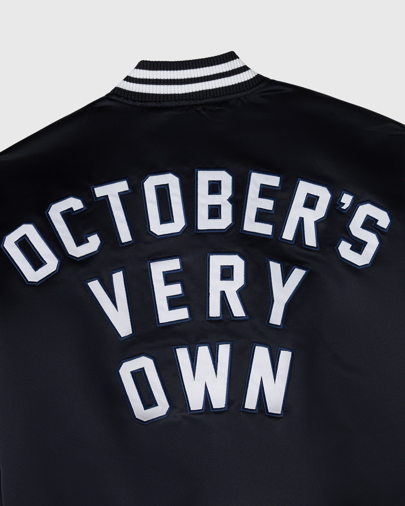 Navy varsity jacket with white "October's Very Own" lettering and black and white striped ribbed collar.