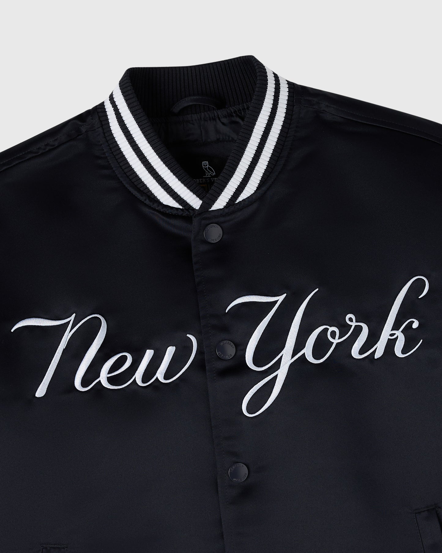 Navy varsity jacket with white "New York" script across chest, white striped ribbed collar, and button front closure.