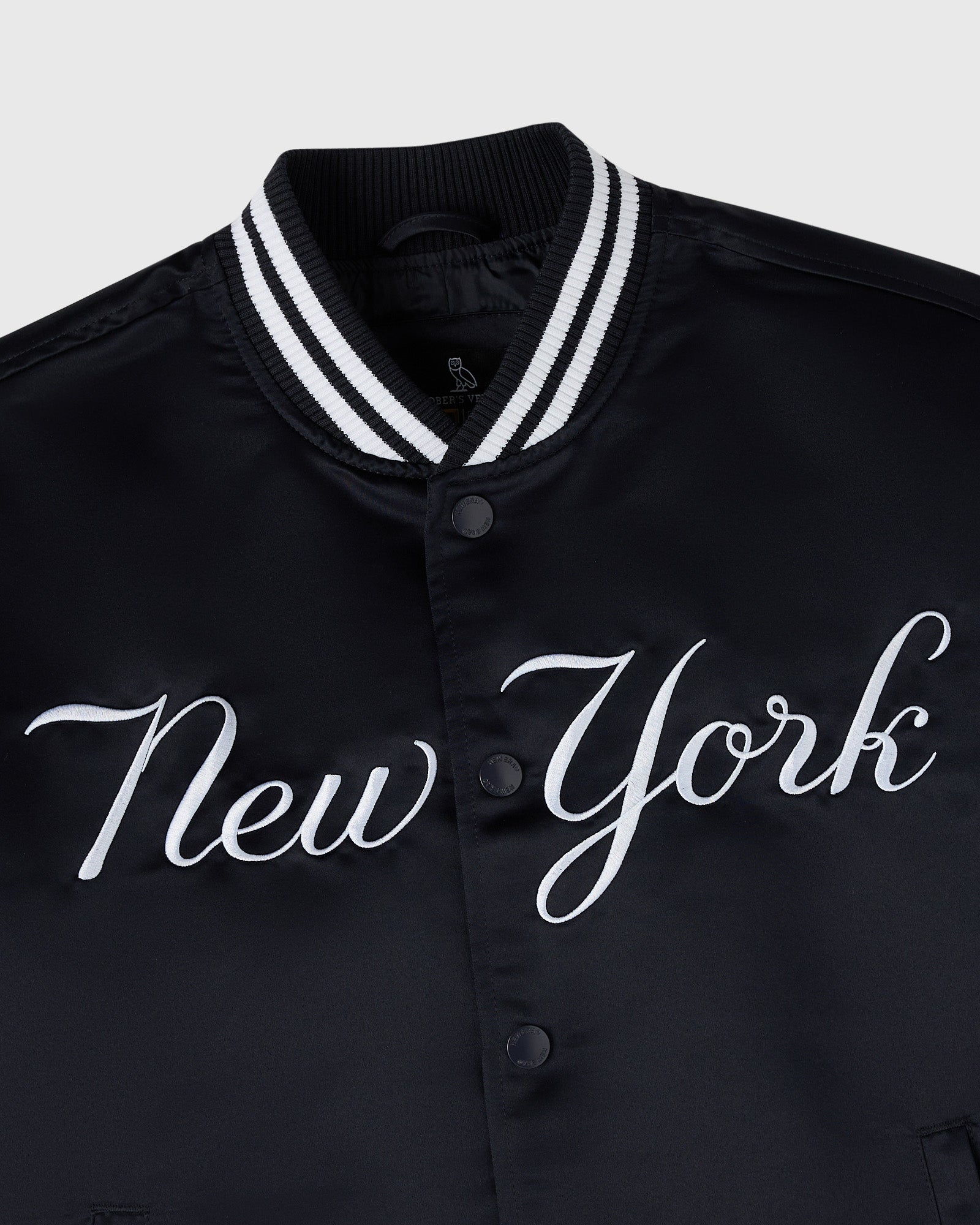 Navy varsity jacket with white "New York" script across chest, white striped ribbed collar, and button front closure.
