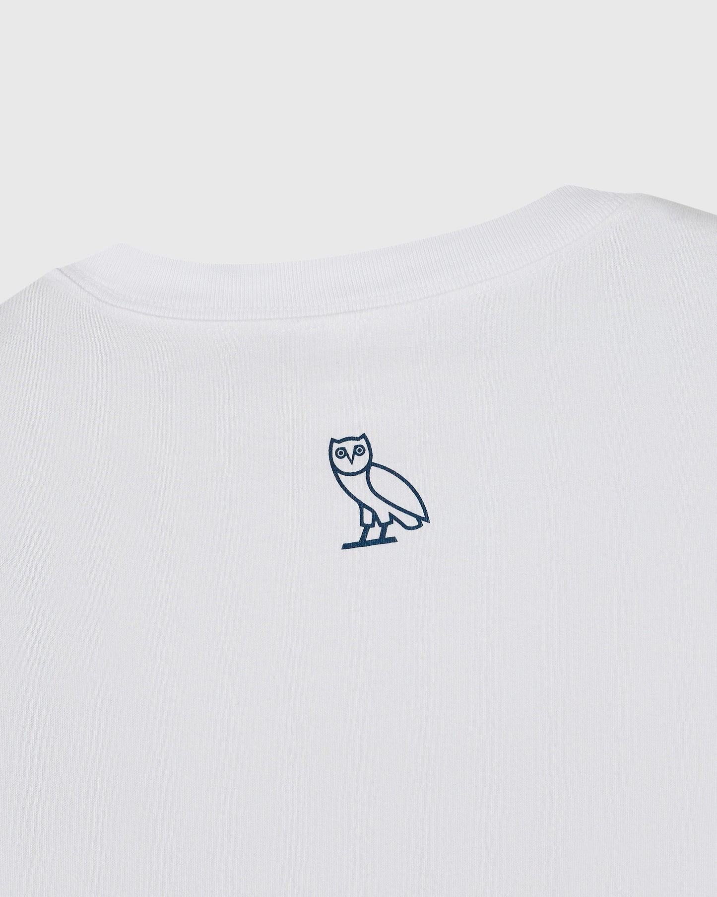 White t-shirt with small navy owl emblem on chest.