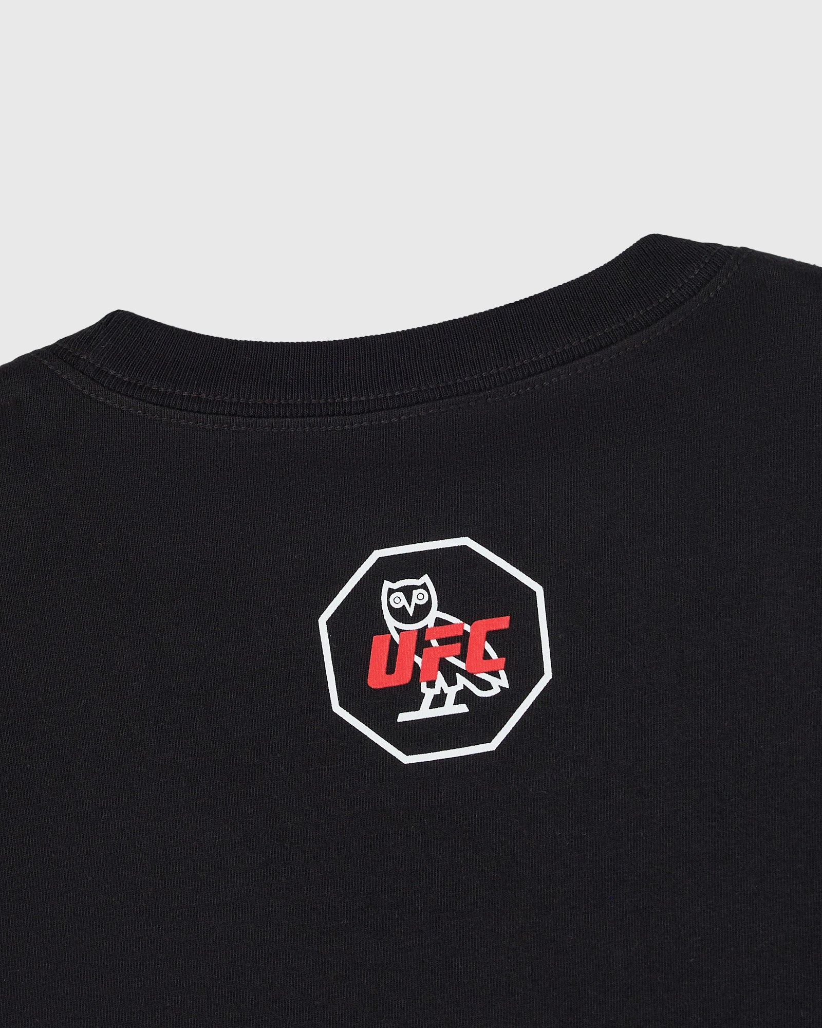 Close up of back of black t-shirt with UFC octagon graphic featuring an owl character in a white octagon logo with red text on chest.