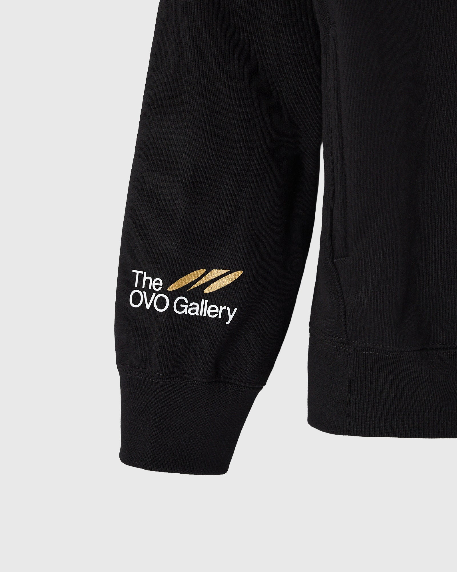 Black hoodie with "The OVO Gallery" logo and gold feather graphic printed on left sleeve.