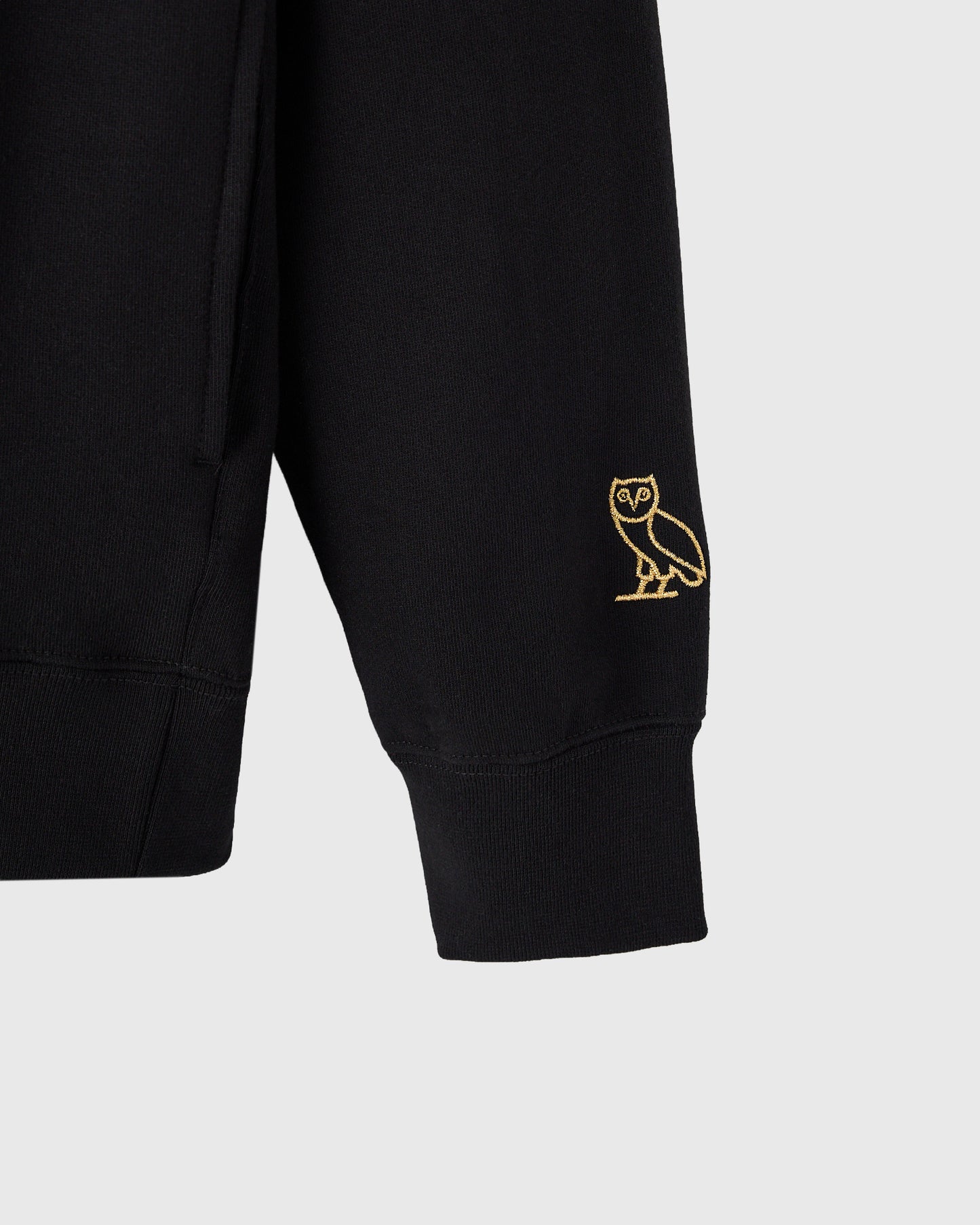 Black hoodie with gold owl embroidery on sleeve.