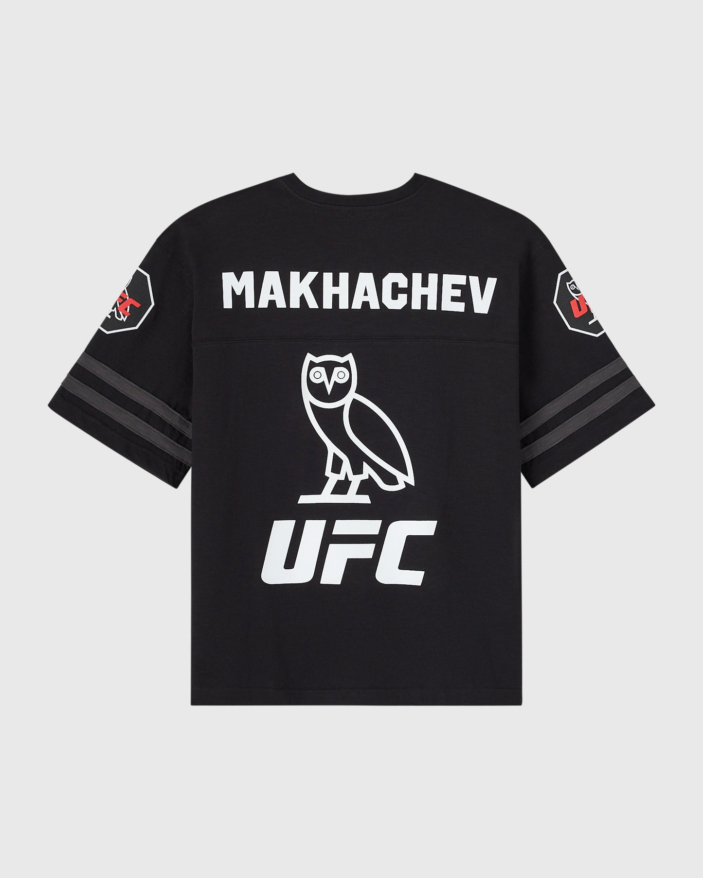 Black short-sleeve tee with white "MAKHACHEV" text, owl graphic, and UFC logo on back; striped sleeves with side patches.