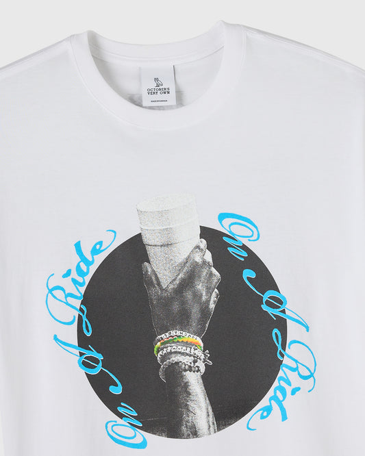 White crewneck tee with black and white photo of hand holding stone wrapped in blue circular text graphic.
