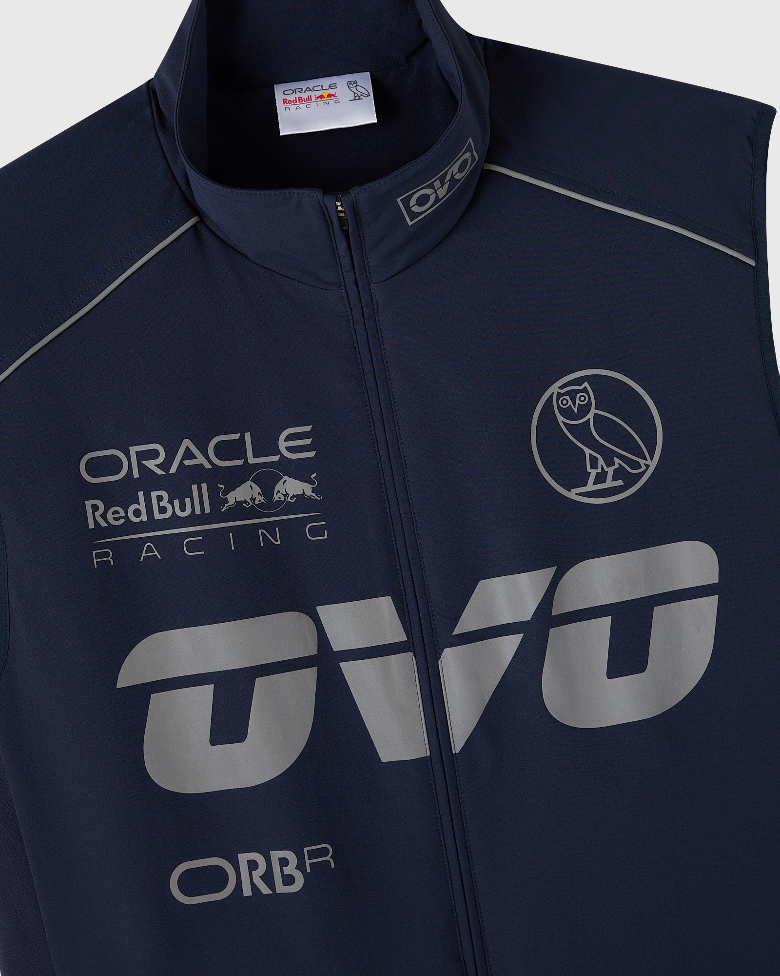 Navy nylon vest with reflective Oracle Red Bull Racing logos, owl graphic, and piping details.